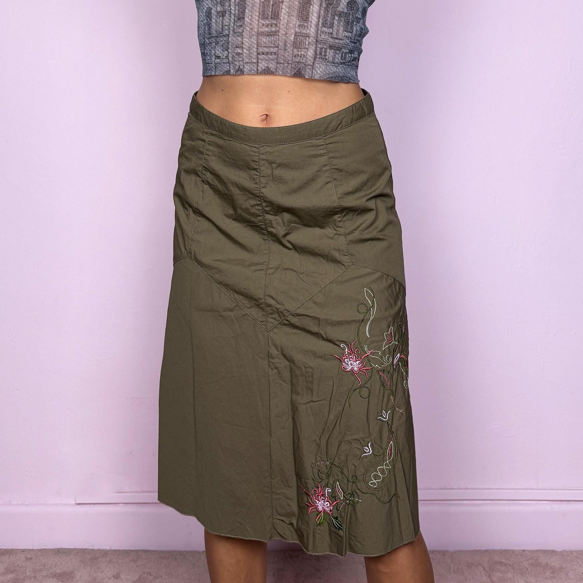 This vintage 2000s khaki green midi skirt features a soft flared silhouette with floral embroidered details and a back zipper closure. Made from cotton, it’s flowy, breathable, and perfect for summer or office wear. It can be styled low-rise on XXS or mid/high-rise on XS, offering versatile fit and effortless elegance. Excellent vintage condition.