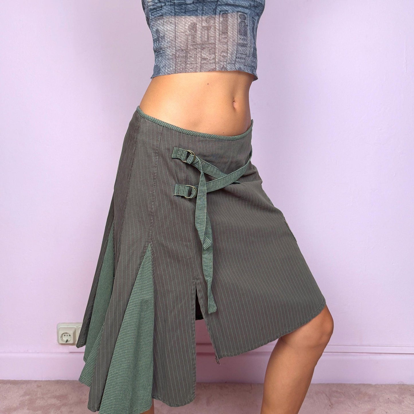 This vintage 2000s khaki green midi skirt features an asymmetric godet-style hem with a side slit, one pocket, and check plaid strap details. Designed with a side zipper closure, it channels deconstructed avant-garde energy with a fairycore-grunge twist. Can be worn low-rise on XS–S or high-rise on M for versatile styling. Made from 100% cotton fabric. Excellent vintage condition.