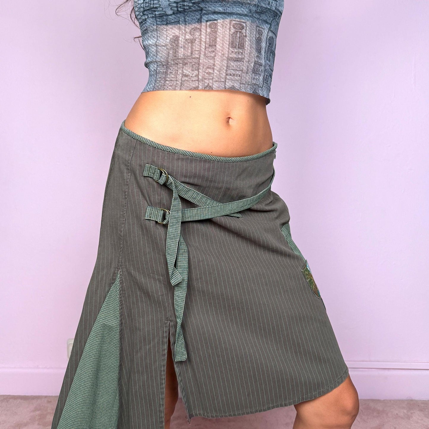 This vintage 2000s khaki green midi skirt features an asymmetric godet-style hem with a side slit, one pocket, and check plaid strap details. Designed with a side zipper closure, it channels deconstructed avant-garde energy with a fairycore-grunge twist. Can be worn low-rise on XS–S or high-rise on M for versatile styling. Made from 100% cotton fabric. Excellent vintage condition.