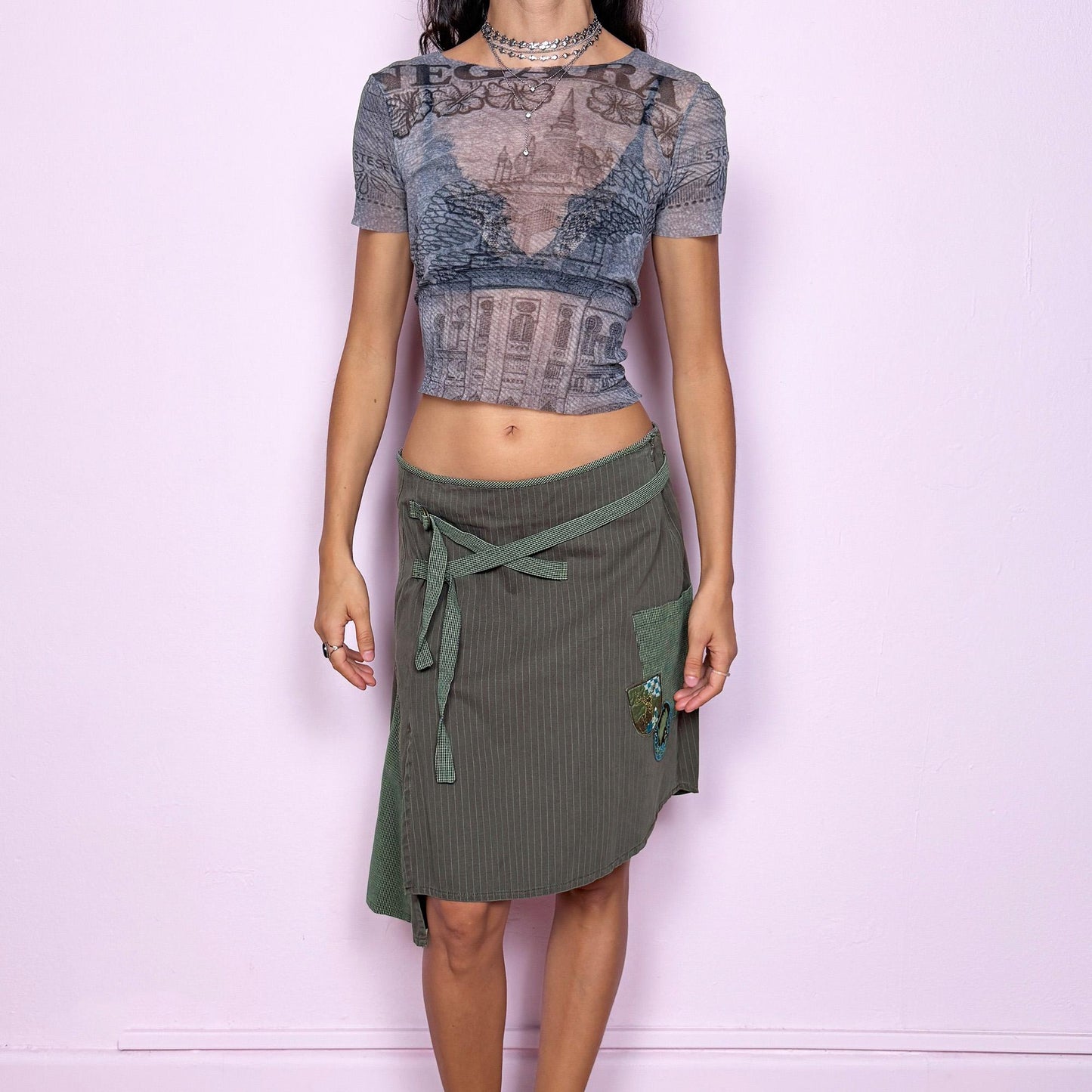 This vintage 2000s khaki green midi skirt features an asymmetric godet-style hem with a side slit, one pocket, and check plaid strap details. Designed with a side zipper closure, it channels deconstructed avant-garde energy with a fairycore-grunge twist. Can be worn low-rise on XS–S or high-rise on M for versatile styling. Made from 100% cotton fabric. Excellent vintage condition.