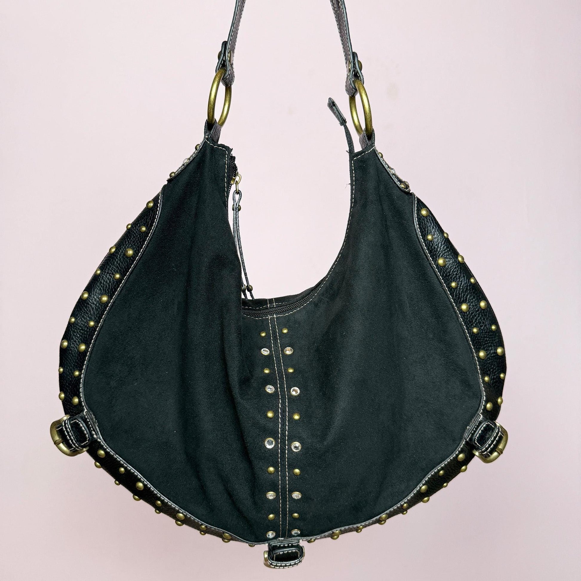 This vintage 2000s black faux suede shoulder bag features a single wide strap, gold metal rings, and rhinestone studs along the curved edges. The sculptural hobo shape and soft structure give it effortless city-girl appeal with Y2K glam flair. Spacious yet refined, it’s perfect for evening outings or street styling. A striking statement accessory. Made from faux suede and faux leather. Excellent vintage condition.