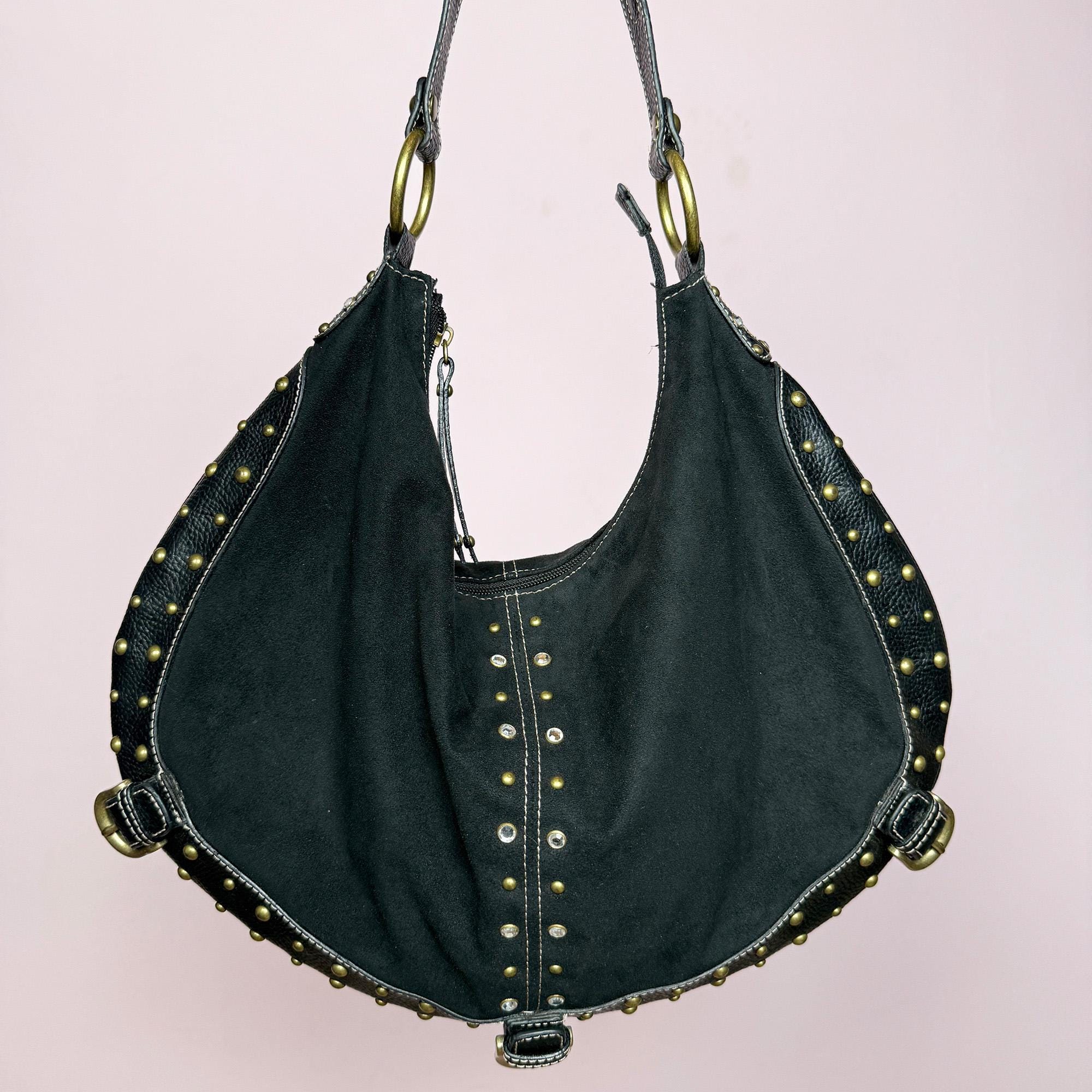 This vintage 2000s black faux suede shoulder bag features a single wide strap, gold metal rings, and rhinestone studs along the curved edges. The sculptural hobo shape and soft structure give it effortless city-girl appeal with Y2K glam flair. Spacious yet refined, it’s perfect for evening outings or street styling. A striking statement accessory. Made from faux suede and faux leather. Excellent vintage condition.