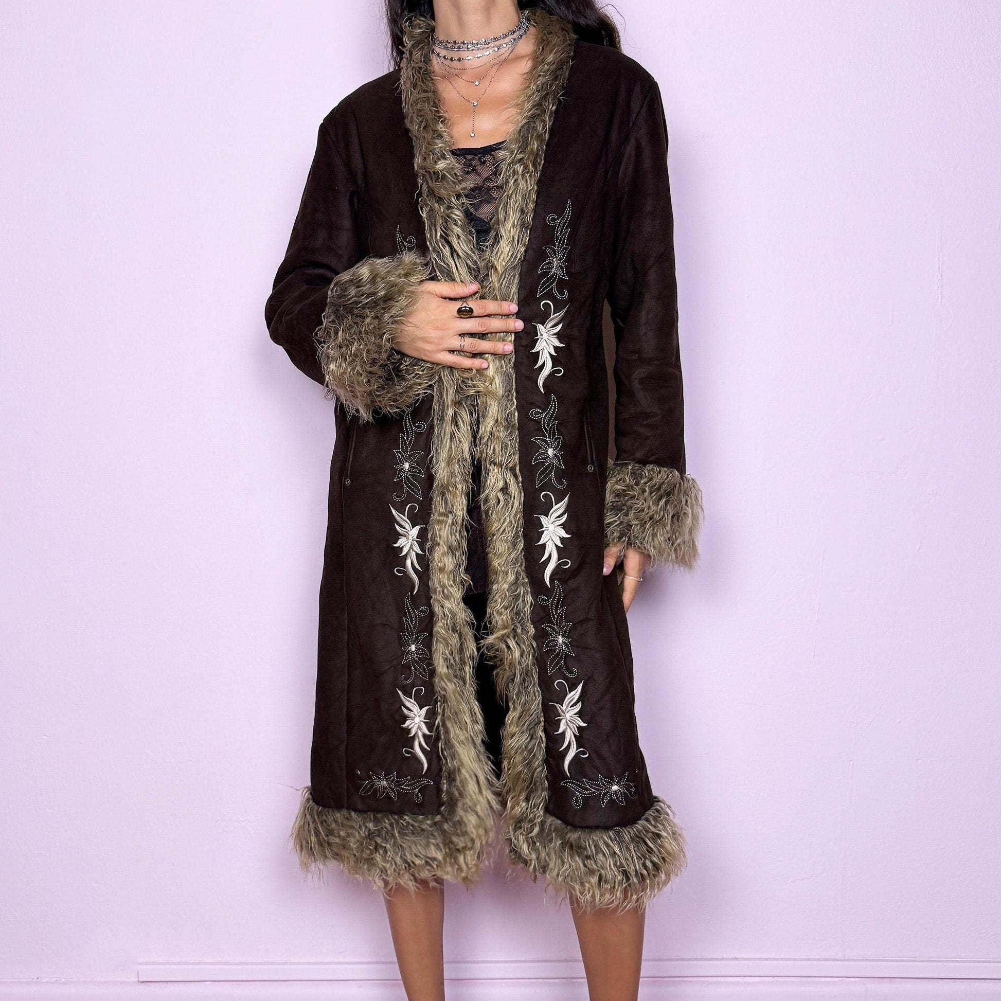 This vintage 2000s dark brown Penny Lane coat features beige faux fur trim at the collar, cuffs, and hem, with intricate floral embroidery along the front. Crafted from soft faux suede with pockets and dual snap-and-hook closure, it embodies the whimsical 70s Afghan-inspired Y2K aesthetic. Warm and romantic—perfect for fairycore, boho, and forest muse styling. Made from polyester faux suede and faux fur. Great vintage condition.