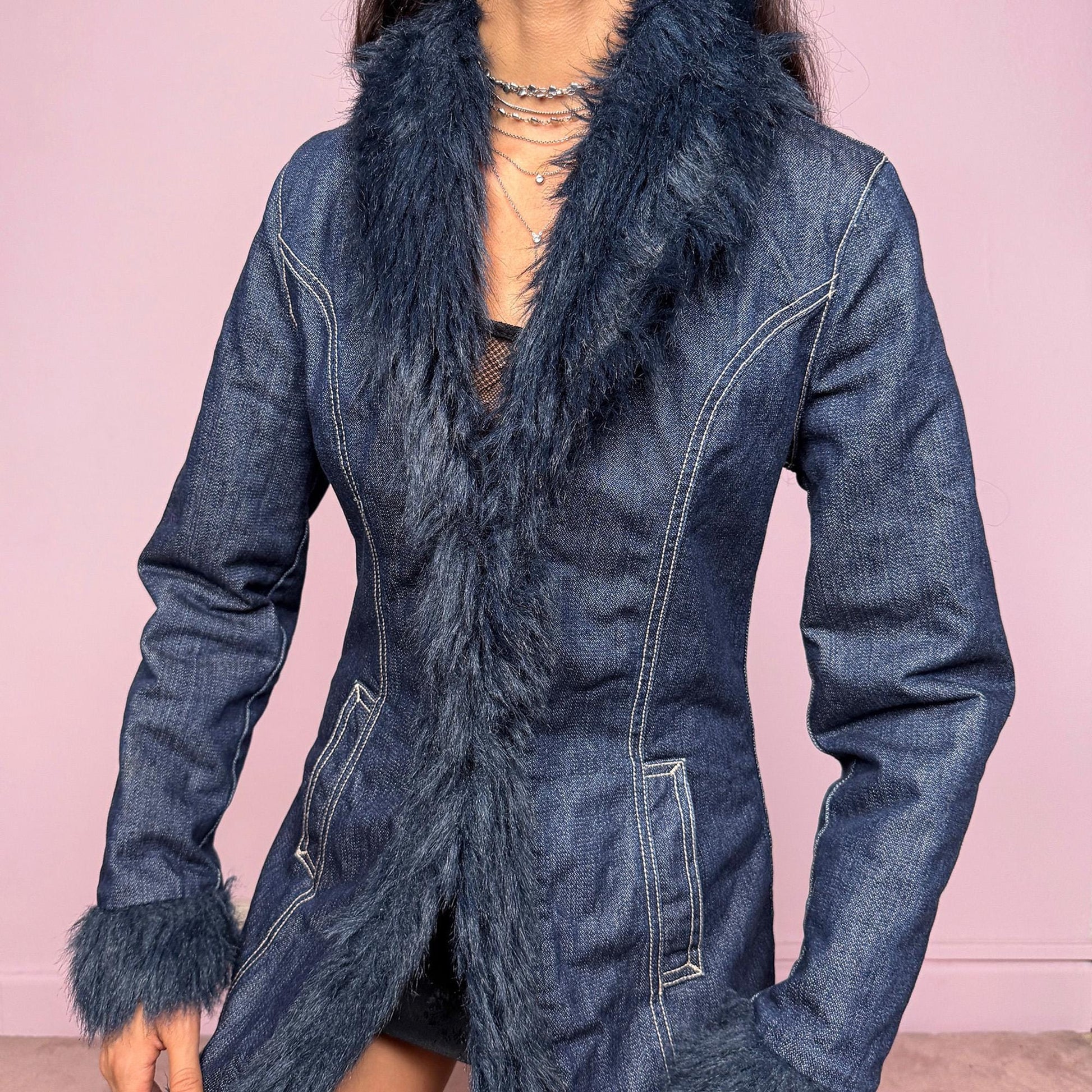 This vintage 2000s dark blue denim Penny Lane coat features deep navy faux fur trim along the collar, cuffs, and hem. Designed with front pockets and button closure, it blends 70s-inspired boho charm with Y2K streetwear edge. The fitted cut and rich indigo tone make it the ultimate statement winter coat—perfect for city styling or retro layering. Made from a cotton polyester denim blend with faux fur trim. Excellent vintage condition.