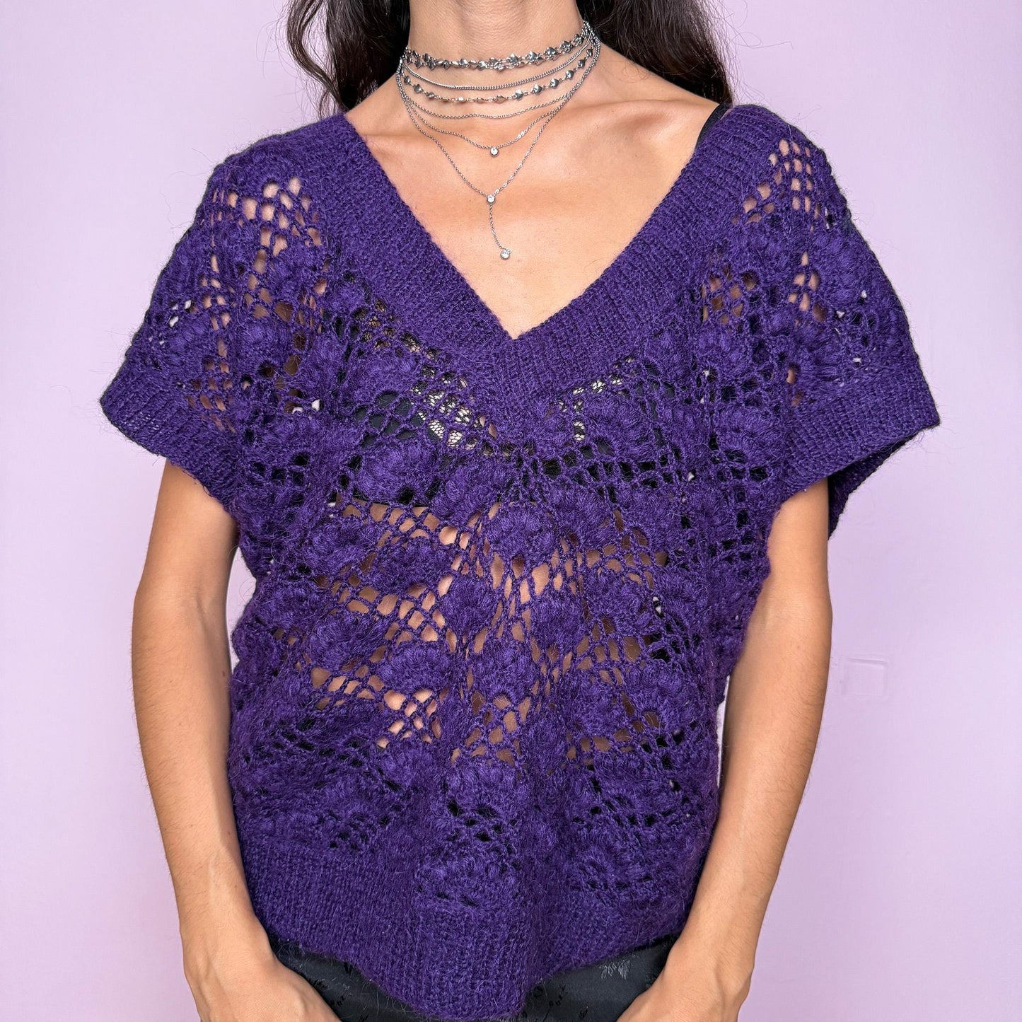 This vintage purple open-knit sweater vest features a deep V-neckline and sleeveless cut for versatile styling. Its airy crochet texture offers sheer dimension, ideal for layering over shirts and blouses. A vibrant granny-style knit with a stretchy fit, perfect for fall or winter boho and lounge looks. Excellent vintage condition.