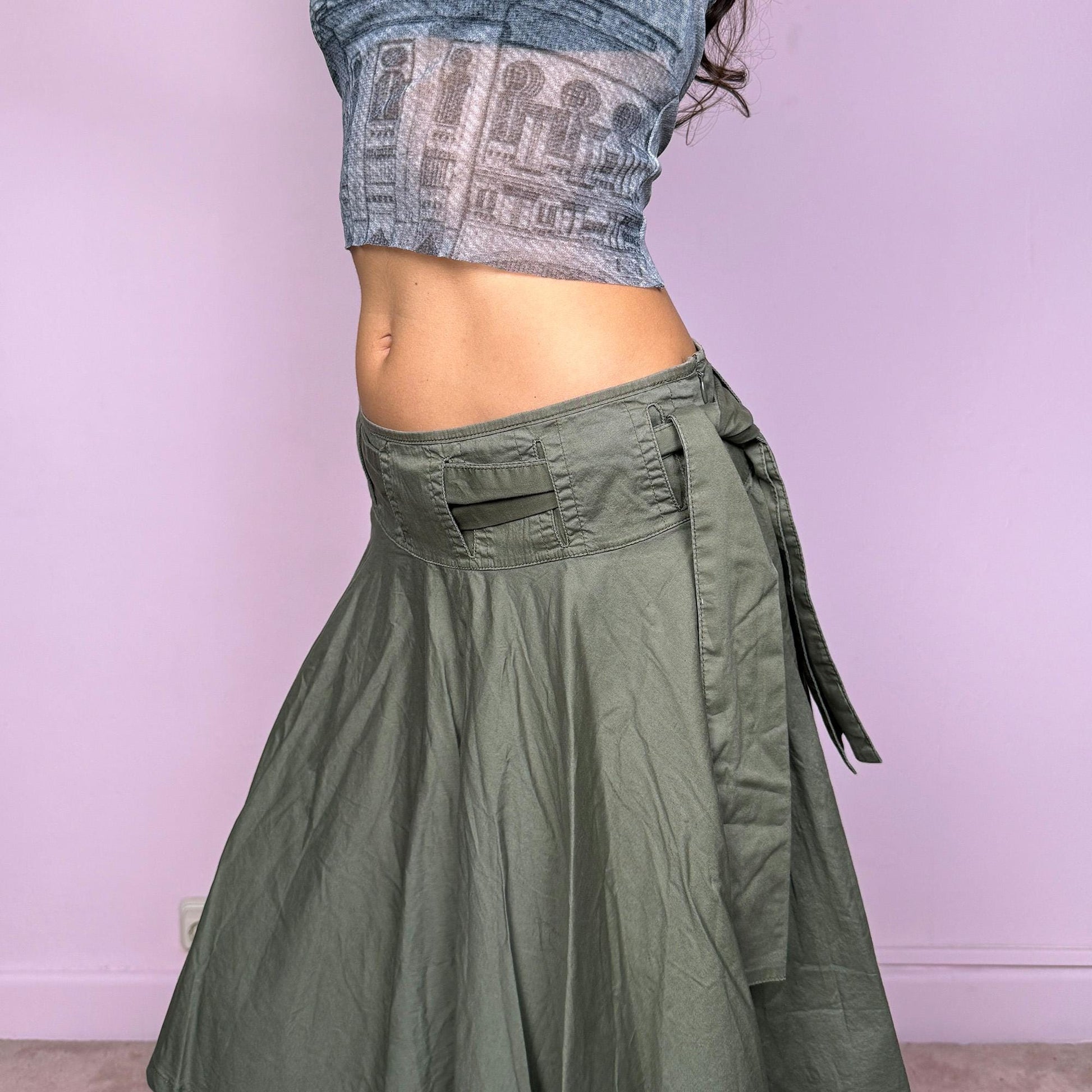 This vintage Y2K khaki green midi skirt features a flared circle silhouette with a side zipper and a removable matching belt that ties elegantly at the side. Designed to sit low-rise, it blends minimalist streetwear with fairycore flow for an effortlessly chic look. Perfect for office wear or summer outings. Made from a soft cotton blend fabric. Excellent vintage condition.