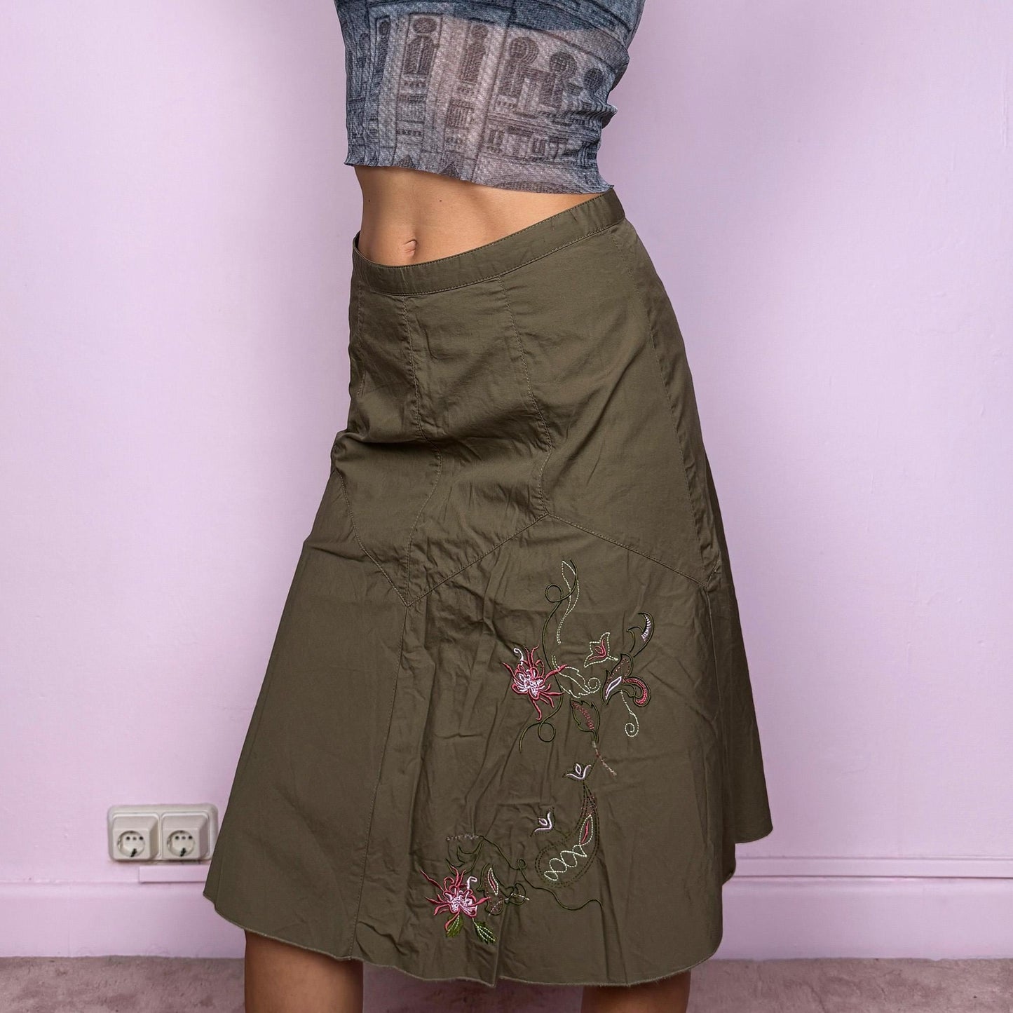 This vintage 2000s khaki green midi skirt features a soft flared silhouette with floral embroidered details and a back zipper closure. Made from cotton, it’s flowy, breathable, and perfect for summer or office wear. It can be styled low-rise on XXS or mid/high-rise on XS, offering versatile fit and effortless elegance. Excellent vintage condition.