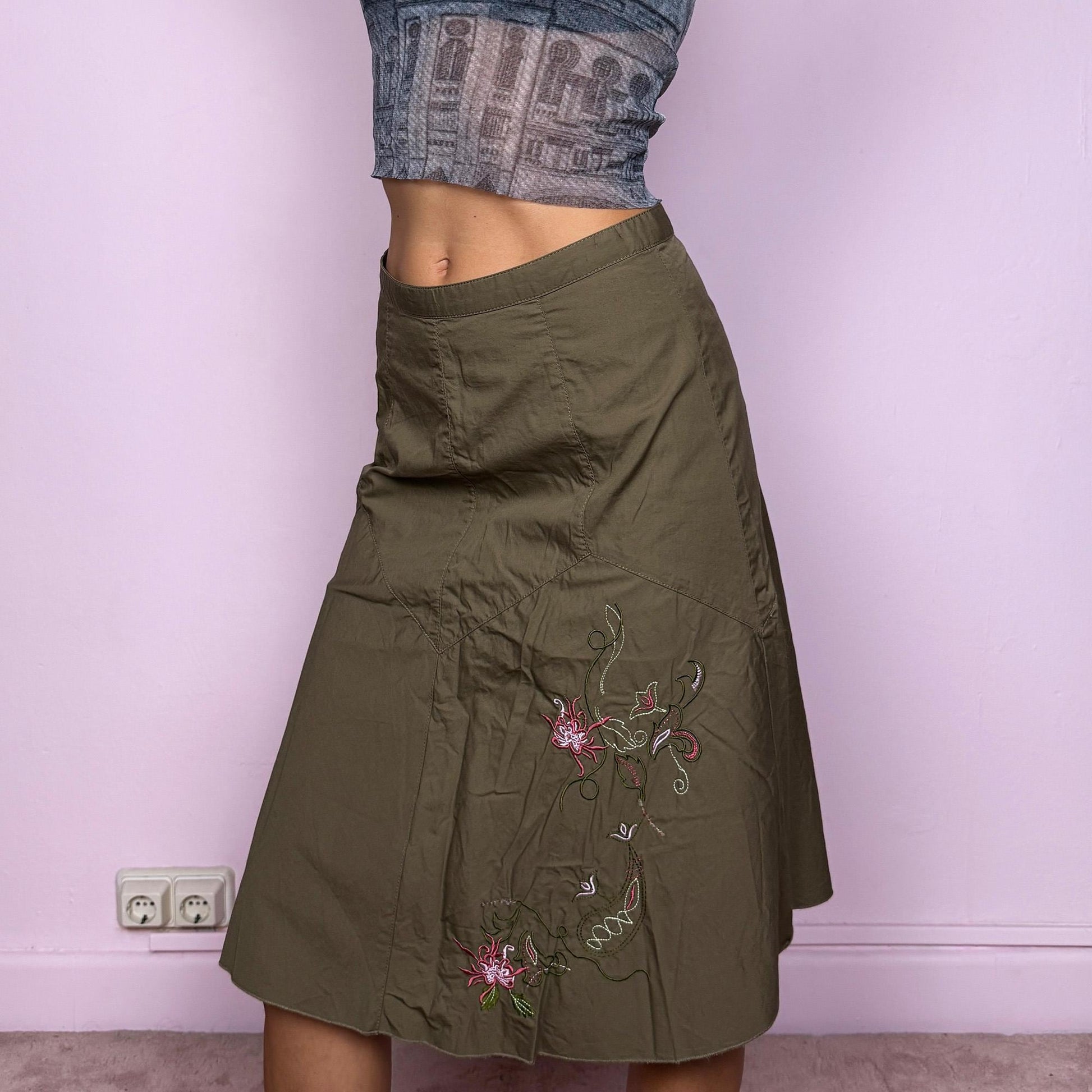 This vintage 2000s khaki green midi skirt features a soft flared silhouette with floral embroidered details and a back zipper closure. Made from cotton, it’s flowy, breathable, and perfect for summer or office wear. It can be styled low-rise on XXS or mid/high-rise on XS, offering versatile fit and effortless elegance. Excellent vintage condition.