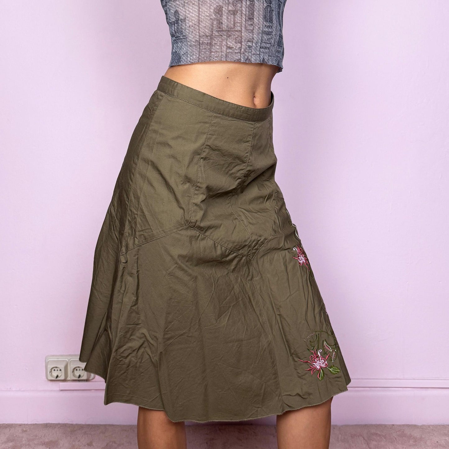 This vintage 2000s khaki green midi skirt features a soft flared silhouette with floral embroidered details and a back zipper closure. Made from cotton, it’s flowy, breathable, and perfect for summer or office wear. It can be styled low-rise on XXS or mid/high-rise on XS, offering versatile fit and effortless elegance. Excellent vintage condition.
