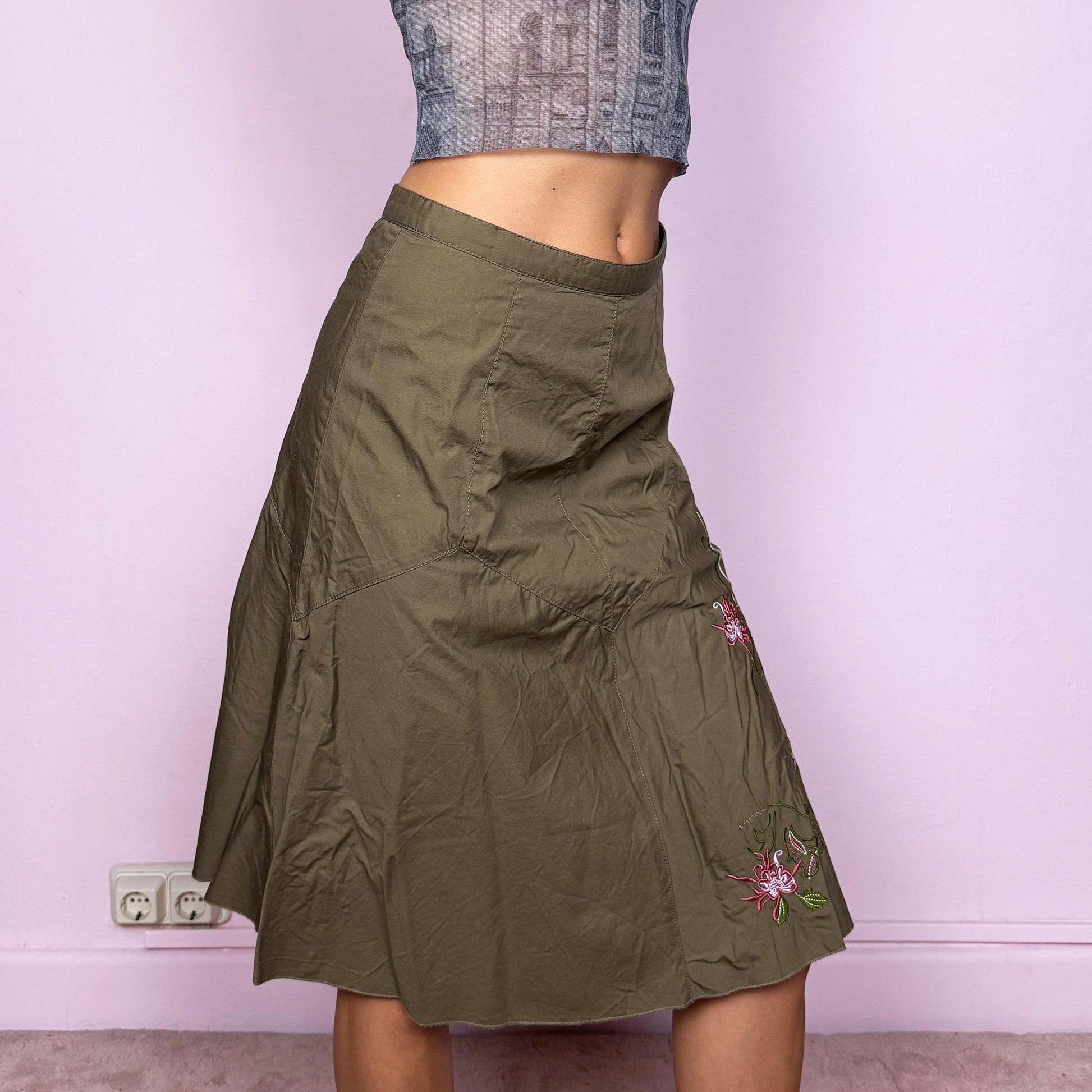 This vintage 2000s khaki green midi skirt features a soft flared silhouette with floral embroidered details and a back zipper closure. Made from cotton, it’s flowy, breathable, and perfect for summer or office wear. It can be styled low-rise on XXS or mid/high-rise on XS, offering versatile fit and effortless elegance. Excellent vintage condition.