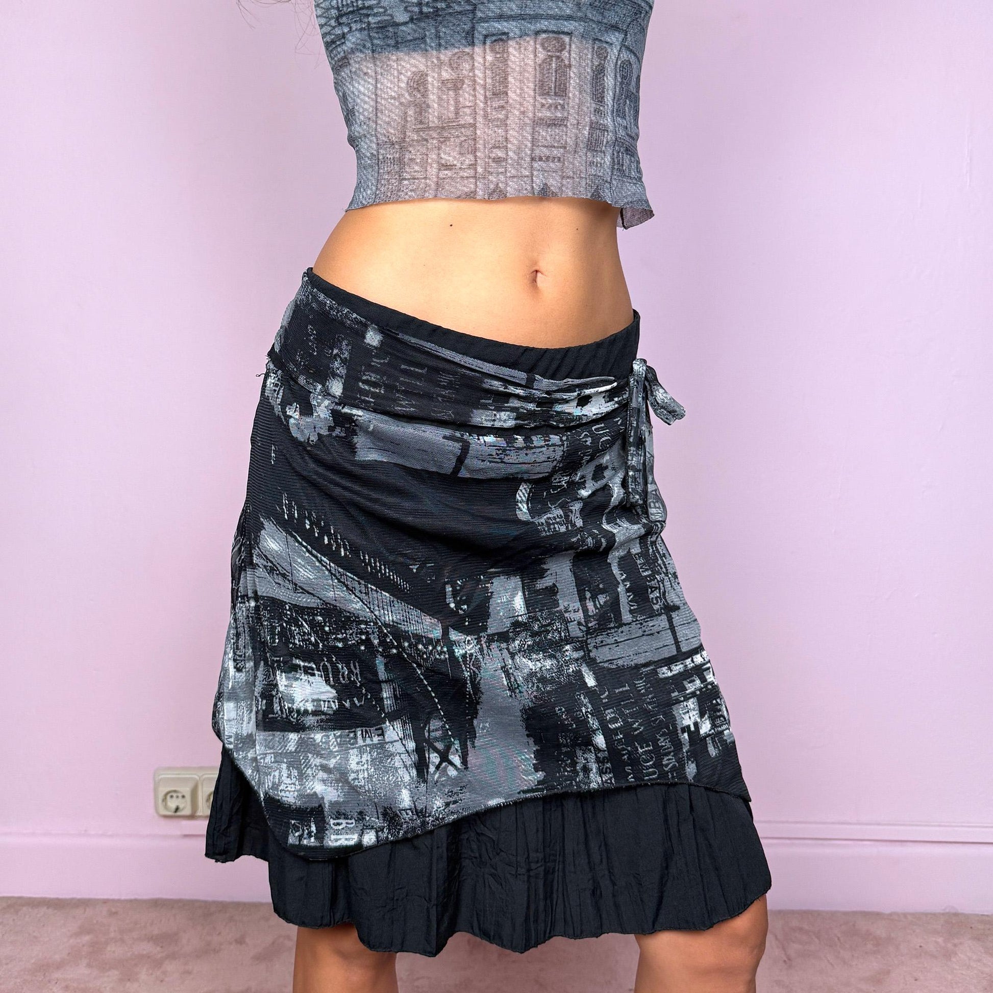 This vintage 2000s black mini skirt features a ruffle hem, side zipper closure, and semi-sheer abstract graphic mesh overlay with a tie-front detail. Its deconstructed, cyber-futuristic silhouette captures the weird girl aesthetic—perfect for night parties or streetwear looks. Can be worn low-rise in L or high-rise in XL for versatile styling. Made from a polyester blend fabric. Great vintage condition.