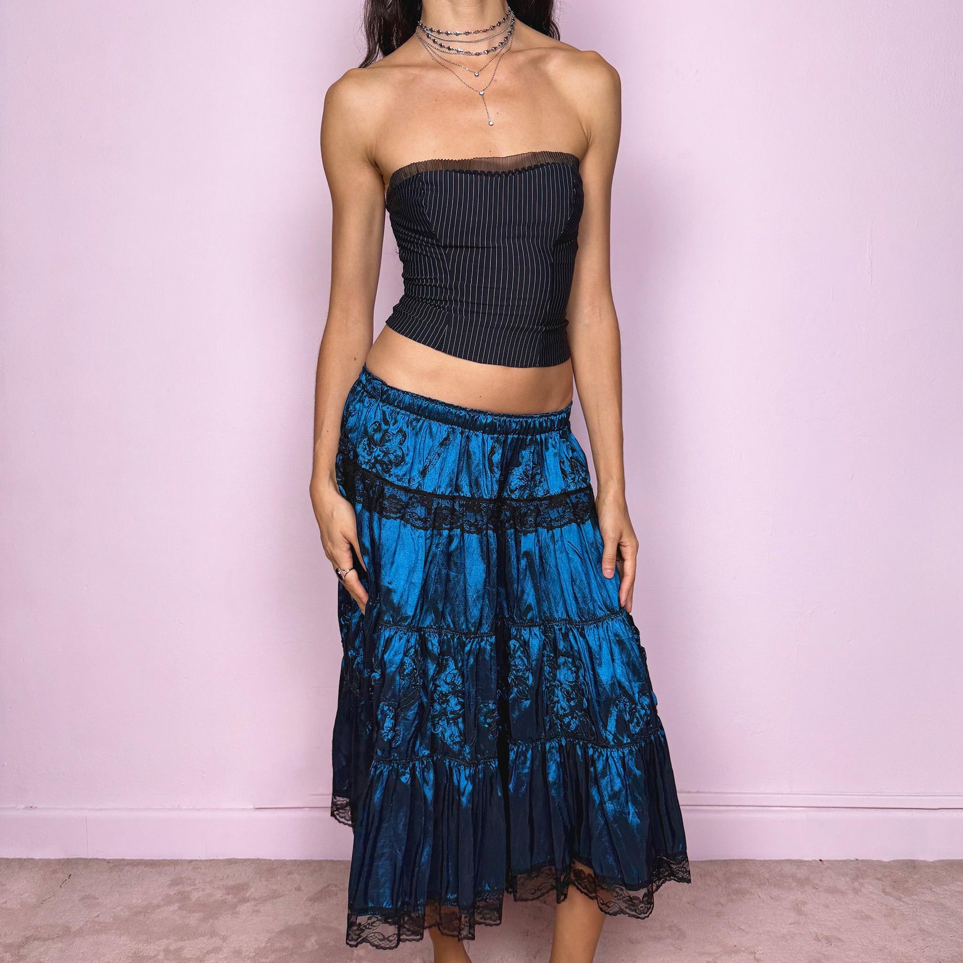 This stunning vintage 90s blue tiered midi skirt features an elastic waist, black lace trims, and delicate applique details for a dreamy, gothic silhouette. The rich sheen and romantic texture evoke dark romance and witchy elegance, perfect for formal nights, parties, or galas. Fits low-rise or high-rise for XS and S sizes. Excellent vintage condition.