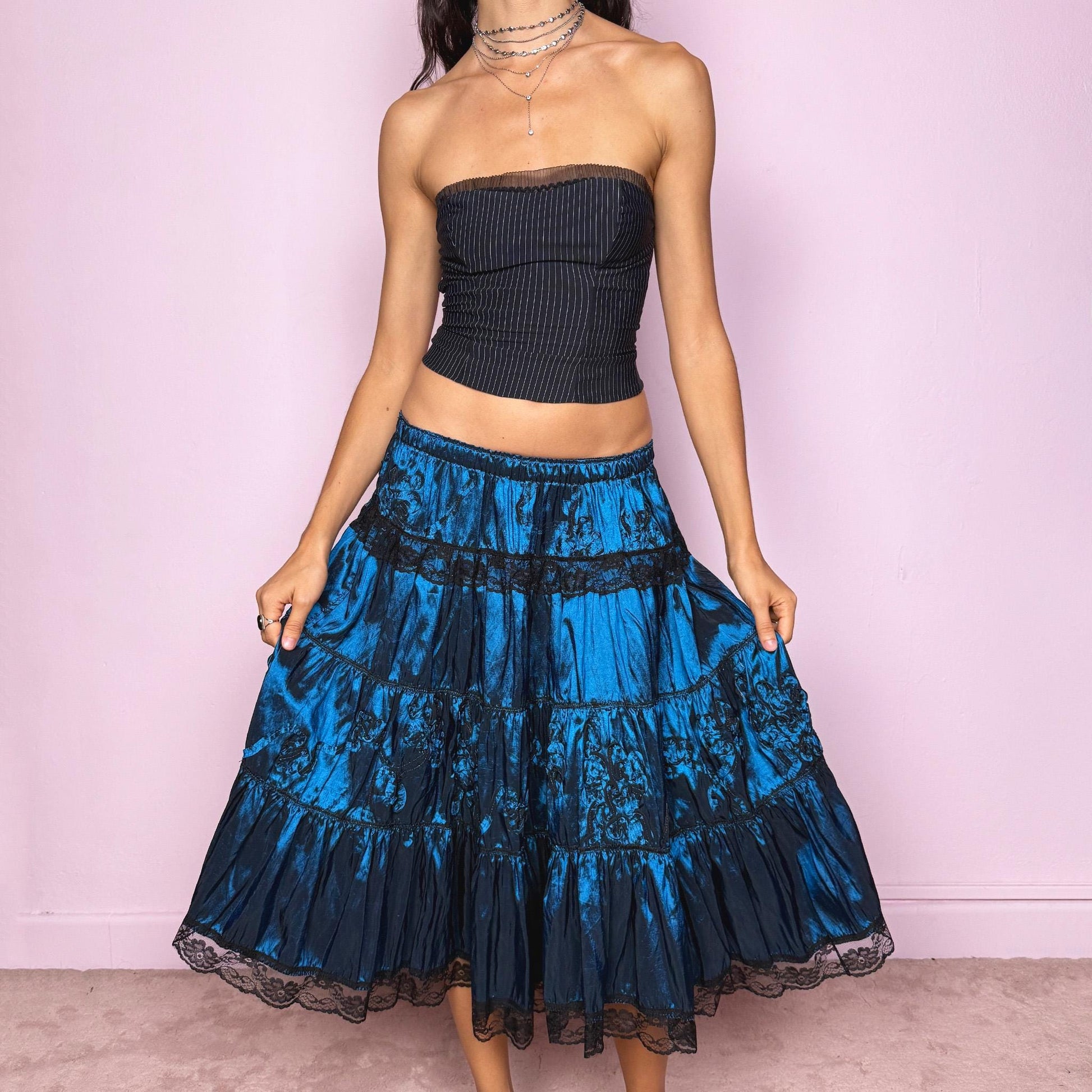 This stunning vintage 90s blue tiered midi skirt features an elastic waist, black lace trims, and delicate applique details for a dreamy, gothic silhouette. The rich sheen and romantic texture evoke dark romance and witchy elegance, perfect for formal nights, parties, or galas. Fits low-rise or high-rise for XS and S sizes. Excellent vintage condition.