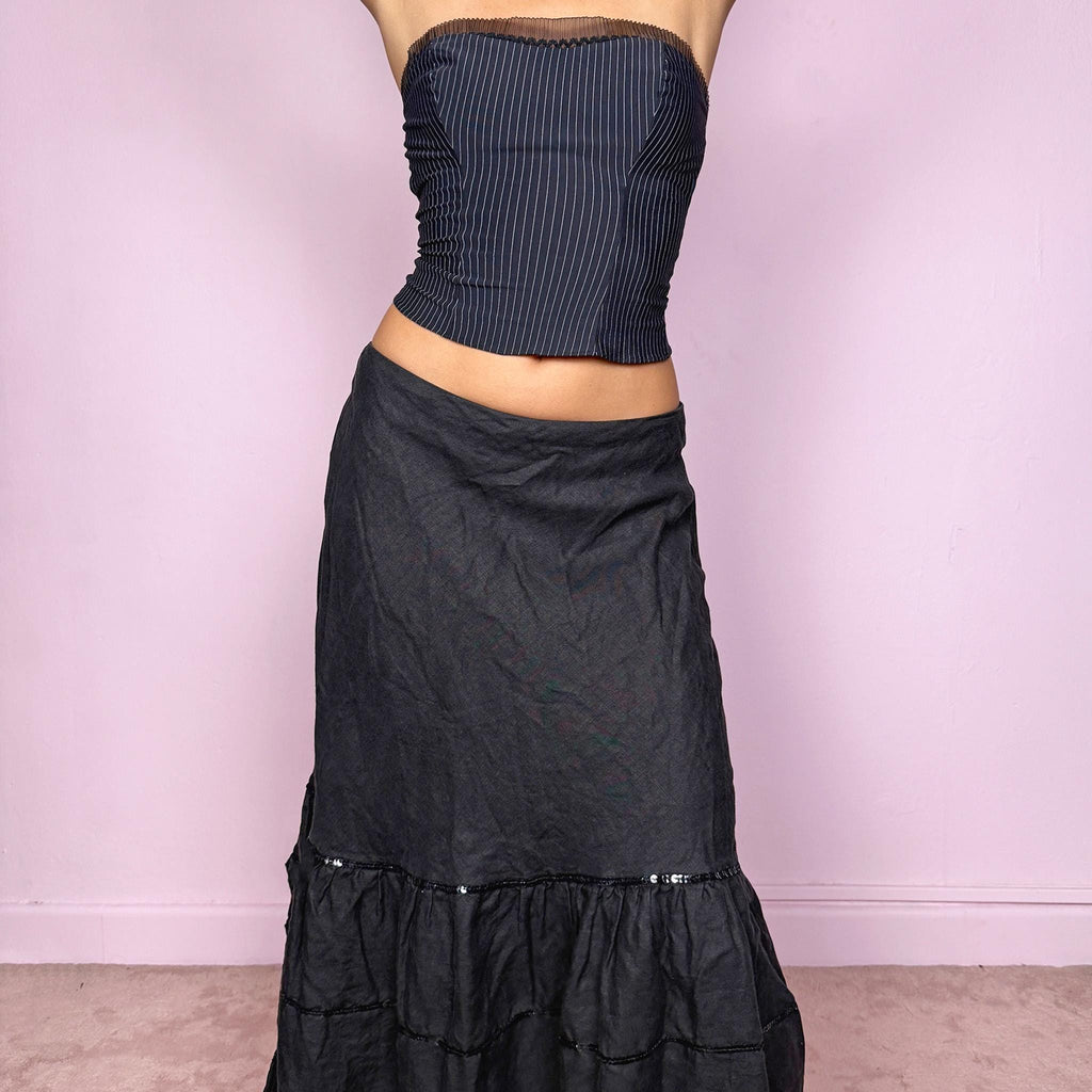This vintage 2000s black linen midi skirt features a tiered ruffle hem, subtle black sequin accents, and a back zipper closure. Made from natural fiber with no stretch, it blends cottagecore charm with witchy goth elegance, perfect for summer or seaside days. Fits mid- to low-rise for size S or high-waisted for size M. French design. Excellent vintage condition.