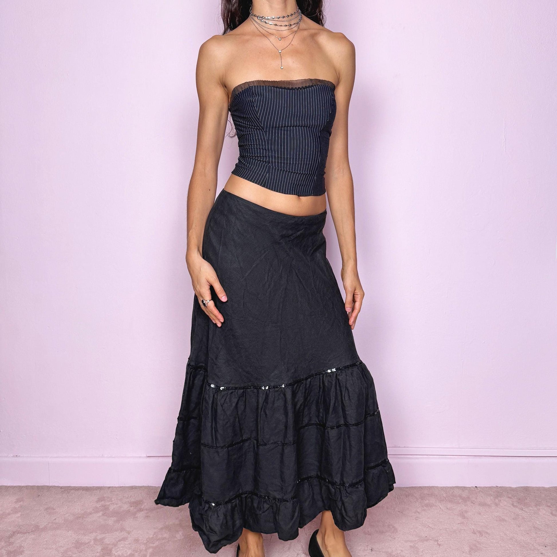 This vintage 2000s black linen midi skirt features a tiered ruffle hem, subtle black sequin accents, and a back zipper closure. Made from natural fiber with no stretch, it blends cottagecore charm with witchy goth elegance, perfect for summer or seaside days. Fits mid- to low-rise for size S or high-waisted for size M. French design. Excellent vintage condition.