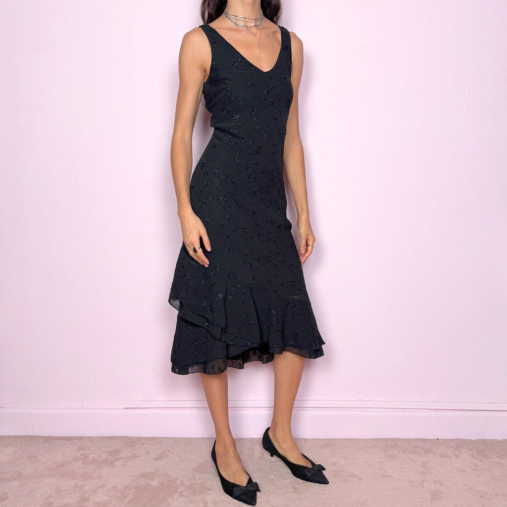 Romantic vintage 2000s black midi dress featuring delicate floral embroidery, a sleeveless cut, a V-neckline and an asymmetrical layered ruffle hem. The slightly stretchy fabric offers a comfortable, flattering fit with a minimal yet elegant look, perfect for a summer night event. Made in Spain from polyester. Excellent vintage condition.