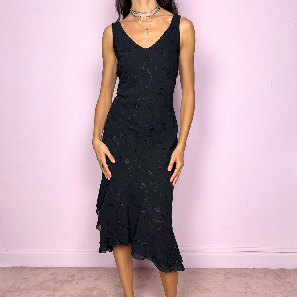 Romantic vintage 2000s black midi dress featuring delicate floral embroidery, a sleeveless cut, a V-neckline and an asymmetrical layered ruffle hem. The slightly stretchy fabric offers a comfortable, flattering fit with a minimal yet elegant look, perfect for a summer night event. Made in Spain from polyester. Excellent vintage condition.
