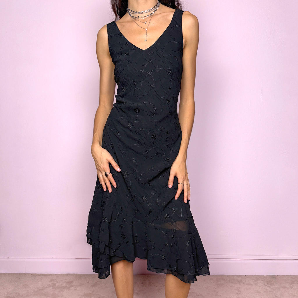 Romantic vintage 2000s black midi dress featuring delicate floral embroidery, a sleeveless cut, a V-neckline and an asymmetrical layered ruffle hem. The slightly stretchy fabric offers a comfortable, flattering fit with a minimal yet elegant look, perfect for a summer night event. Made in Spain from polyester. Excellent vintage condition.