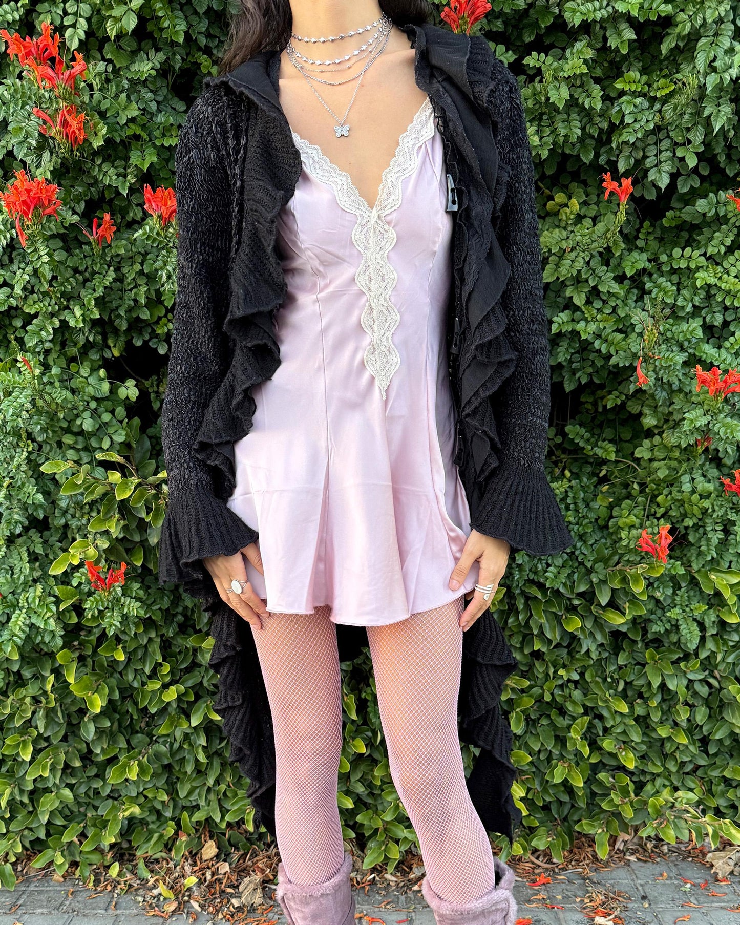 Vintage 2000s black longline cardigan featuring a dramatic ruffle neckline with lace details, bell-sleeve ruffle cuffs and a toggle front closure. The asymmetric pointy hem adds a whimsical, witchy silhouette, while the stretchy cotton–wool–polyamide blend creates a cozy, comfortable fit perfect for winter layering. A stunning fairy-goth statement knit jacket that blends elegance, softness and dark romantic style. Great vintage condition.