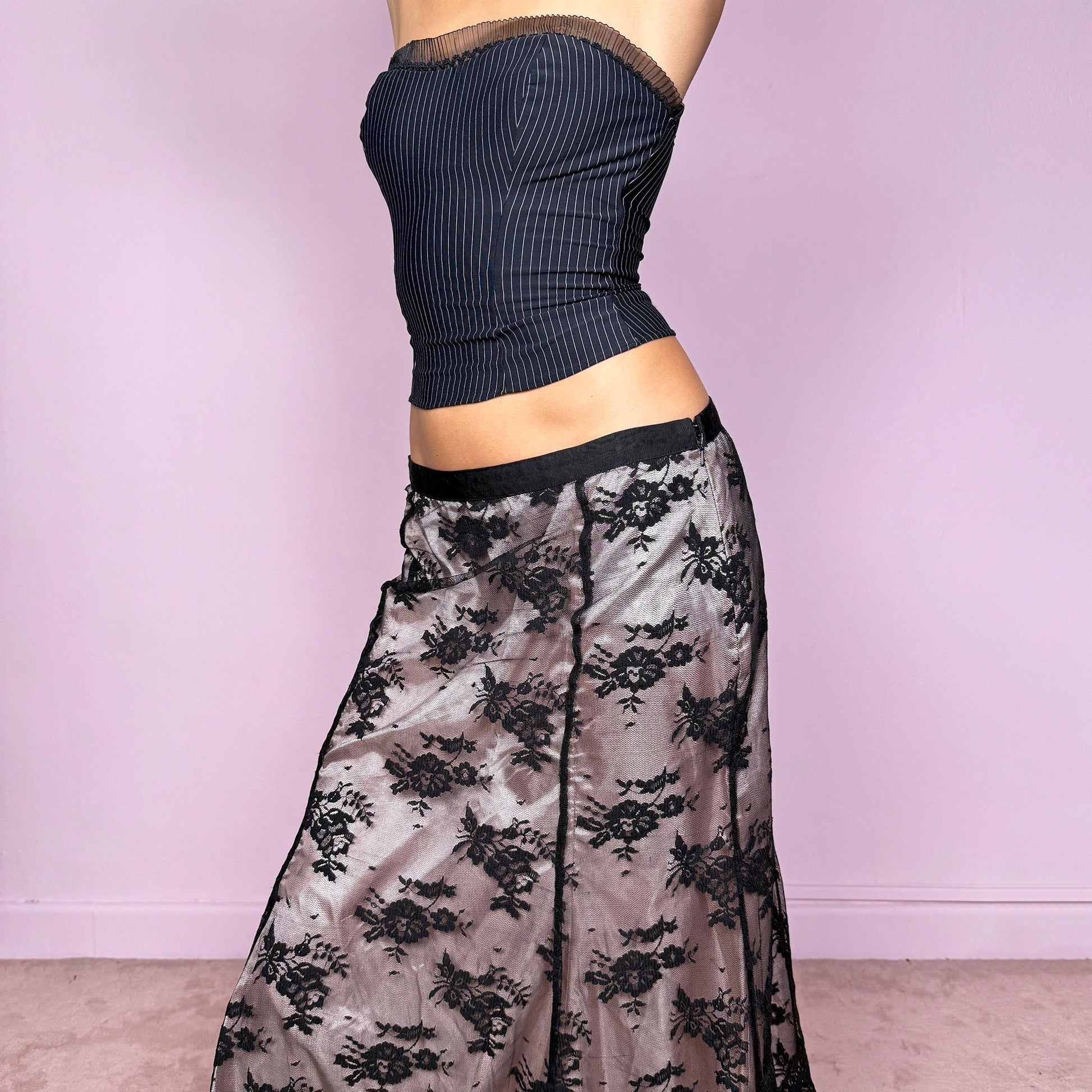 This vintage 2000s midi skirt features delicate black lace overlaying a pale pink lining, creating a stunning dark romantic contrast. Designed with a side zipper closure and no stretch, it perfectly embodies the coquette aesthetic with a touch of elegant sensuality. Ideal for office chic looks, cocktail nights, or romantic dinner dates styled with heels. Fits mid-rise for size M and low-rise for size S. Great vintage condition.