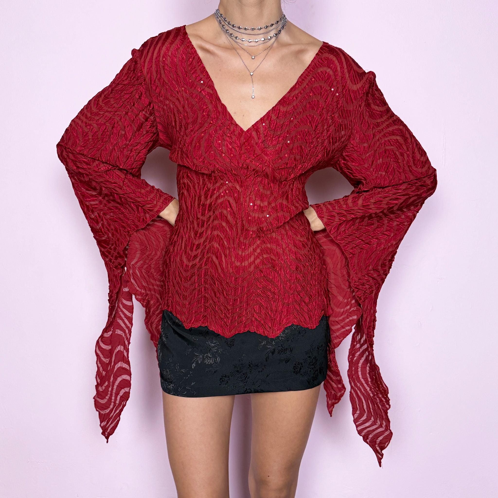 This romantic glam vintage 2000s red blouse features a sheer burnout textured pattern with crinkled wavy detailing and subtle sequins. Designed with a wrap-style silhouette, three-quarter slit dramatic bell sleeves, and an asymmetric hem, it offers a sculpted yet fluid fit ideal for artistic parties, nights out, or editorial avant-garde styling. Made from stretchy polyester. Great vintage condition.