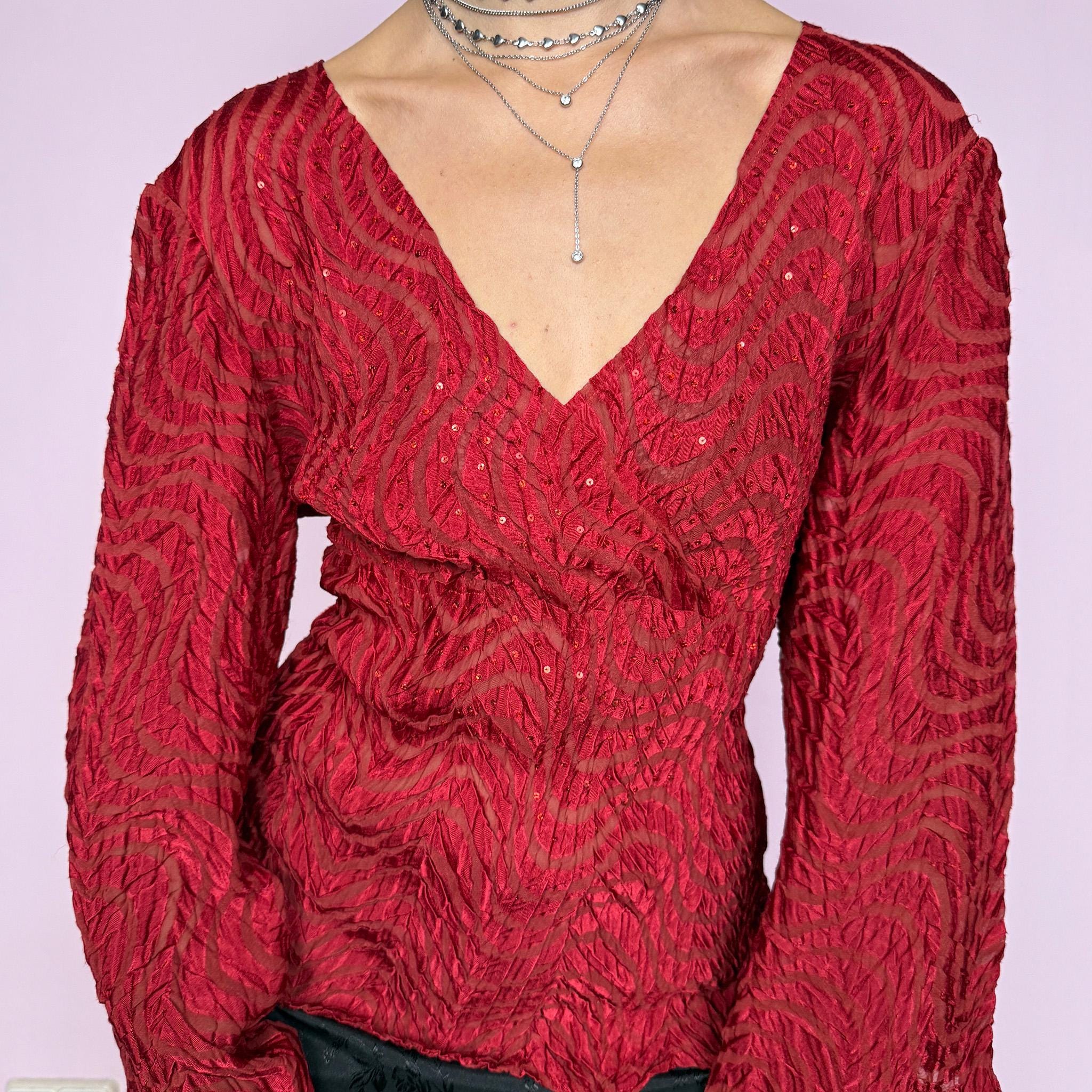 This romantic glam vintage 2000s red blouse features a sheer burnout textured pattern with crinkled wavy detailing and subtle sequins. Designed with a wrap-style silhouette, three-quarter slit dramatic bell sleeves, and an asymmetric hem, it offers a sculpted yet fluid fit ideal for artistic parties, nights out, or editorial avant-garde styling. Made from stretchy polyester. Great vintage condition.