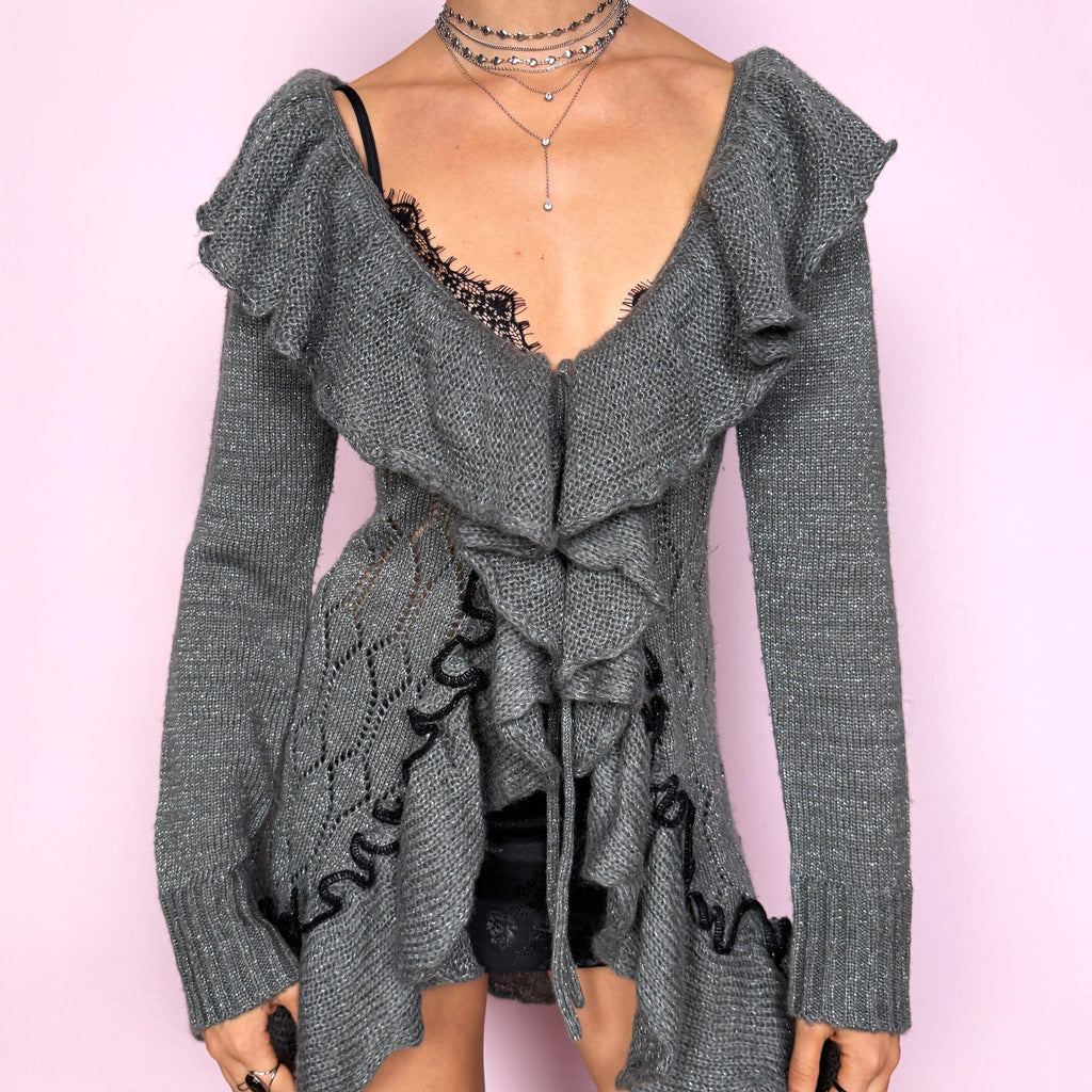 This romantic vintage 2000s gray longline open-knit cardigan features a dramatic ruffle neckline, ruffled hem, and a tie-front closure. The soft, draped silhouette and textured open-knit pattern create a whimsical coquette feel, ideal for autumn layering, winter fairycore styling, or cozy everyday outfits. Made from a stretchy acrylic and mohair blend. Great vintage condition.