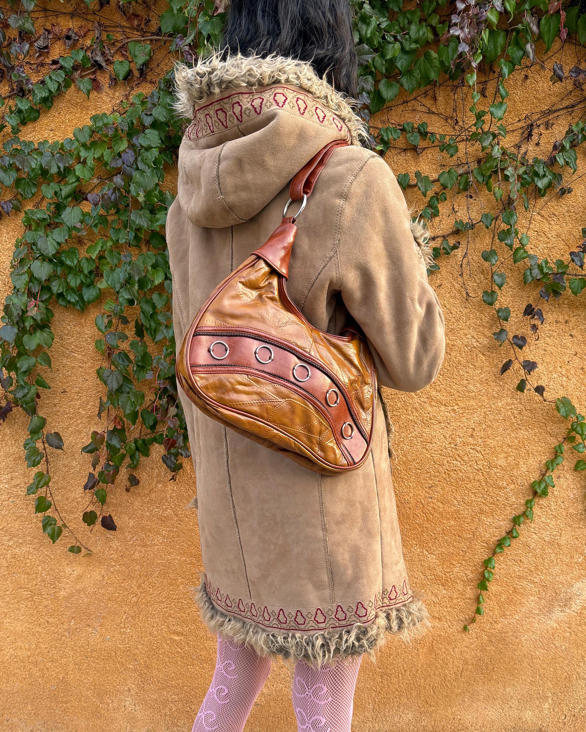Vintage 2000s brown and mustard-brown faux leather shoulder bag with classic Y2K city-girl appeal. Features metal O-ring details across the front, contrast paneling, and a secure double zip closure. The slouchy silhouette makes it perfect as a bold 2000s statement everyday bag or a party-night accessory. Excellent vintage condition.
