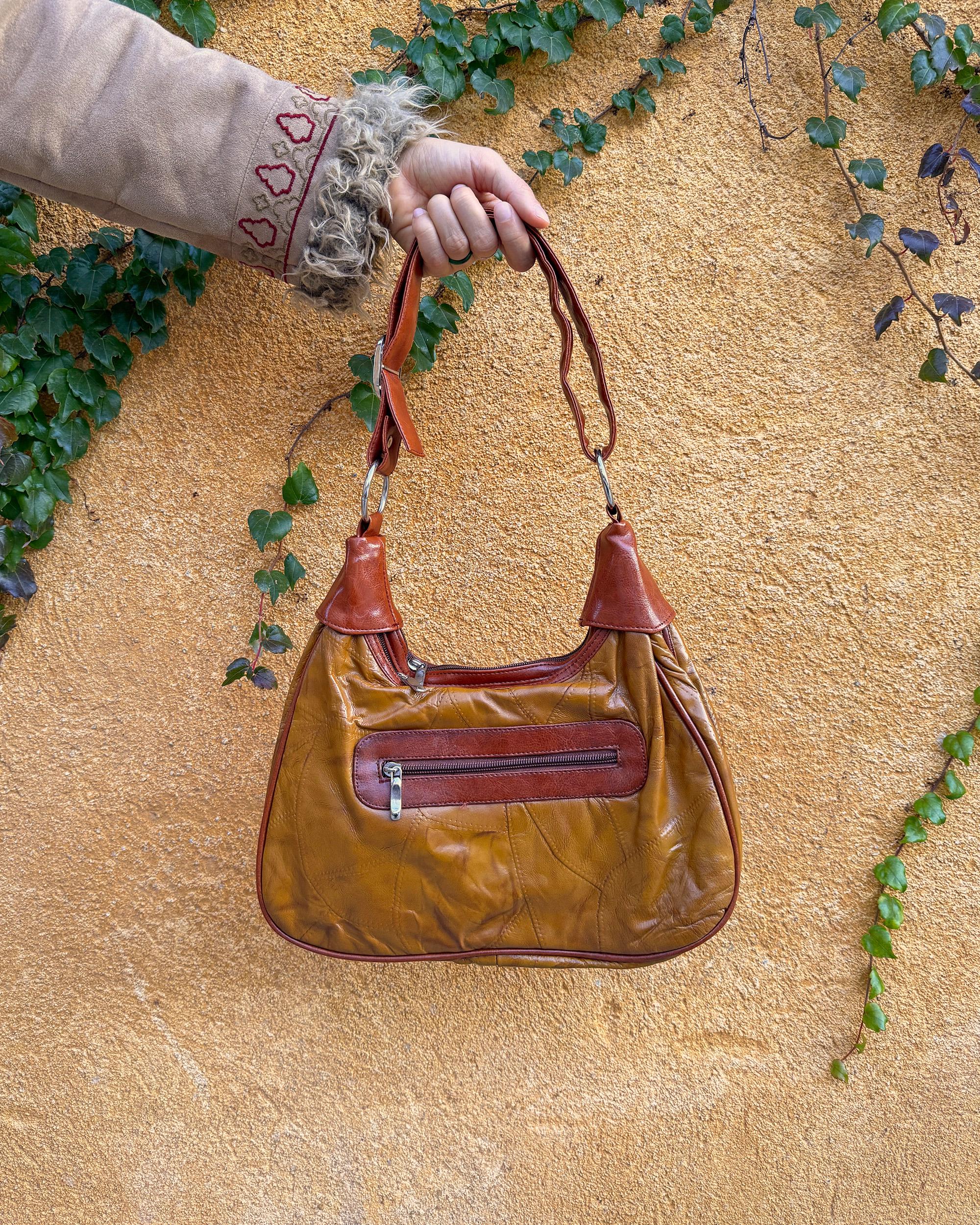 Vintage 2000s brown and mustard-brown faux leather shoulder bag with classic Y2K city-girl appeal. Features metal O-ring details across the front, contrast paneling, and a secure double zip closure. The slouchy silhouette makes it perfect as a bold 2000s statement everyday bag or a party-night accessory. Excellent vintage condition.