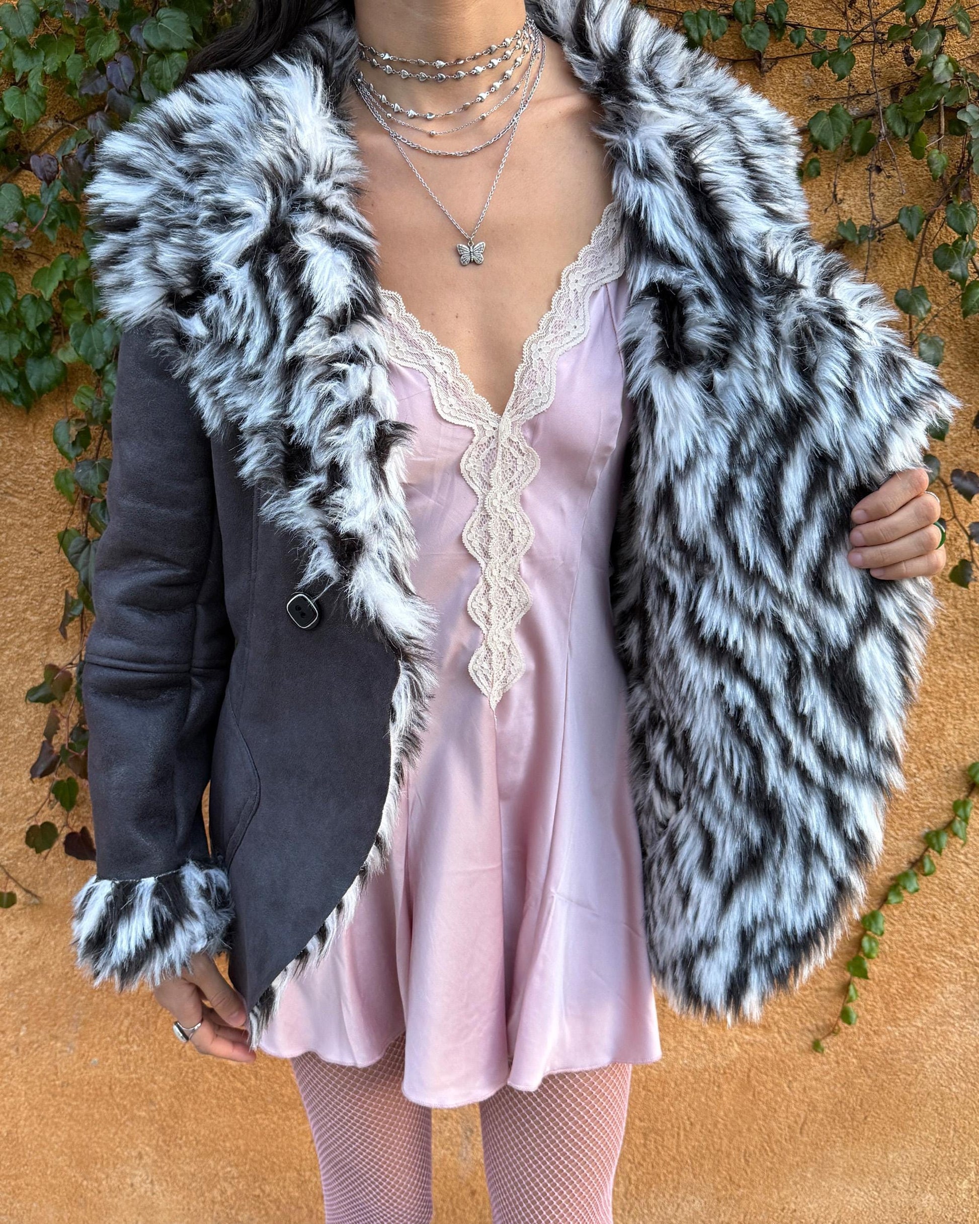 Vintage 2000s dark gray, almost black faux leather Penny Lane jacket with bold faux fur lining at the collar, cuffs, and hem in a black-and-white zebra-inspired pattern. Features a double row of buttons and side pockets. The dramatic fur trim gives it an iconic Y2K glam look, perfect for party nights or bold winter styling. Warm, comfortable, and eye-catching with strong 2000s attitude. Made from a polyester acrylic blend. Excellent vintage condition.