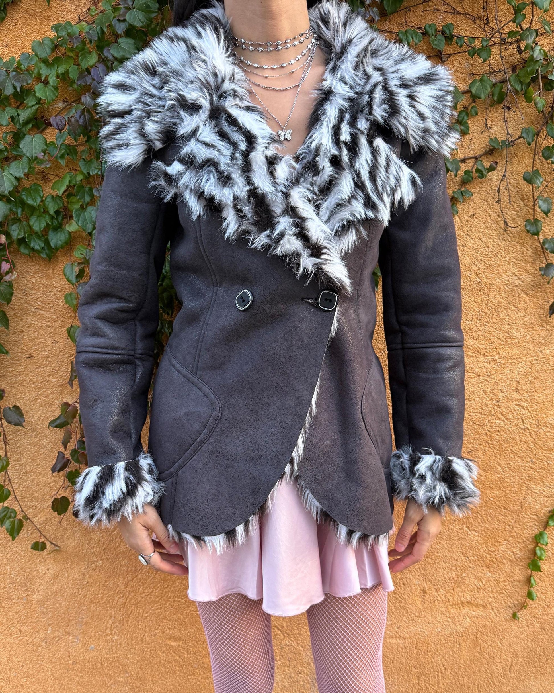 Vintage 2000s dark gray, almost black faux leather Penny Lane jacket with bold faux fur lining at the collar, cuffs, and hem in a black-and-white zebra-inspired pattern. Features a double row of buttons and side pockets. The dramatic fur trim gives it an iconic Y2K glam look, perfect for party nights or bold winter styling. Warm, comfortable, and eye-catching with strong 2000s attitude. Made from a polyester acrylic blend. Excellent vintage condition.