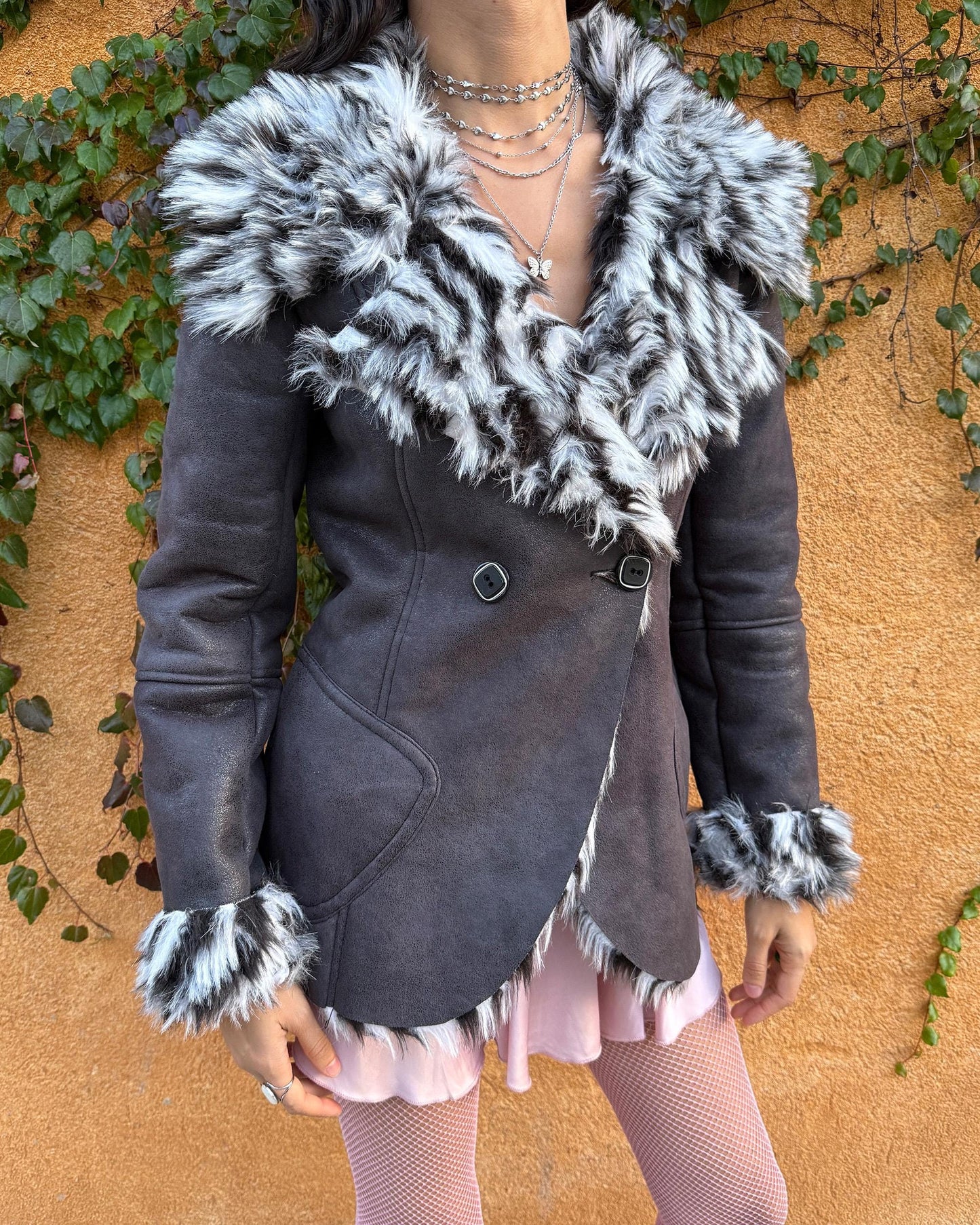 Vintage 2000s dark gray, almost black faux leather Penny Lane jacket with bold faux fur lining at the collar, cuffs, and hem in a black-and-white zebra-inspired pattern. Features a double row of buttons and side pockets. The dramatic fur trim gives it an iconic Y2K glam look, perfect for party nights or bold winter styling. Warm, comfortable, and eye-catching with strong 2000s attitude. Made from a polyester acrylic blend. Excellent vintage condition.