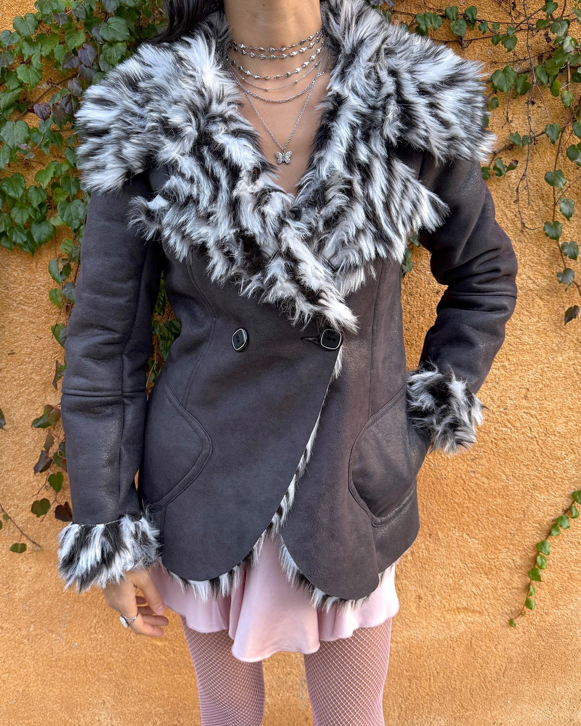 Vintage 2000s dark gray, almost black faux leather Penny Lane jacket with bold faux fur lining at the collar, cuffs, and hem in a black-and-white zebra-inspired pattern. Features a double row of buttons and side pockets. The dramatic fur trim gives it an iconic Y2K glam look, perfect for party nights or bold winter styling. Warm, comfortable, and eye-catching with strong 2000s attitude. Made from a polyester acrylic blend. Excellent vintage condition.