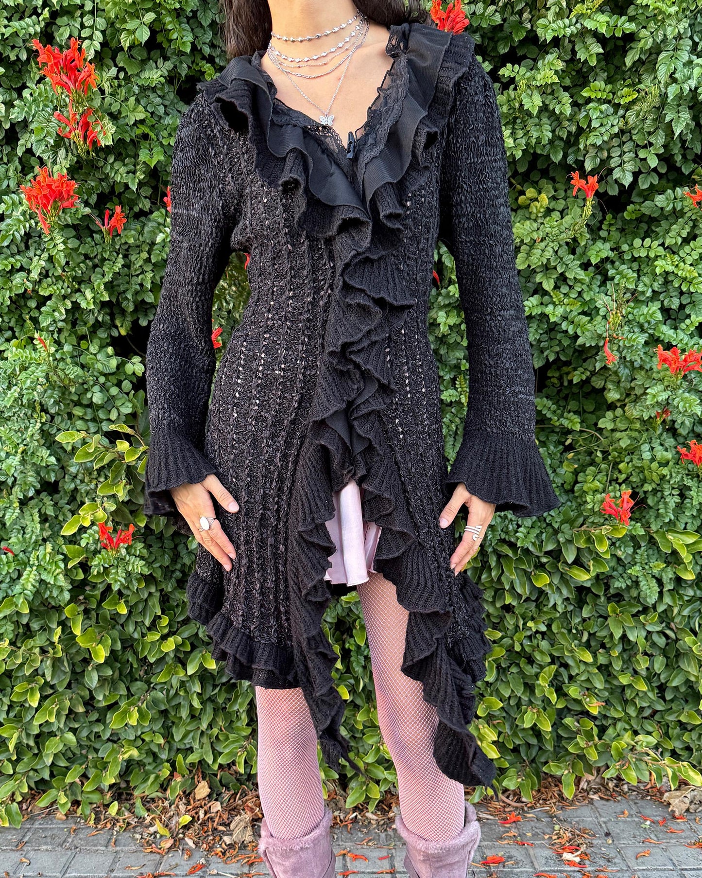 Vintage 2000s black longline cardigan featuring a dramatic ruffle neckline with lace details, bell-sleeve ruffle cuffs and a toggle front closure. The asymmetric pointy hem adds a whimsical, witchy silhouette, while the stretchy cotton–wool–polyamide blend creates a cozy, comfortable fit perfect for winter layering. A stunning fairy-goth statement knit jacket that blends elegance, softness and dark romantic style. Great vintage condition.