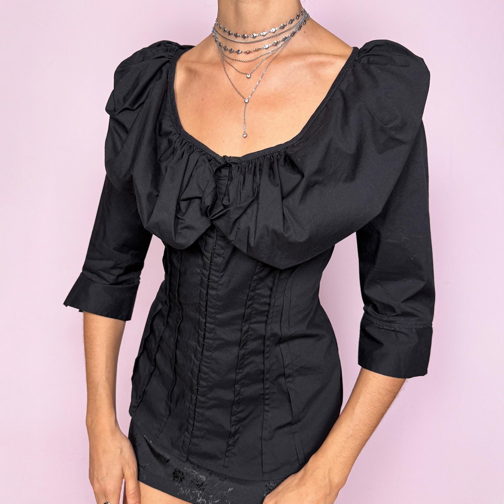 This dark avant garde vintage 2000s black blouse features a dramatic voluminous collared ruffle, a fitted pleated bodice, and three-quarter sleeves. Designed with a minimalist statement approach, it includes subtle mini hook closures and a slightly stretchy cotton–polyamide blend for a structured yet comfortable fit. The sculpted silhouette makes it ideal for formal evening looks, elegant night parties, or polished day-to-office styling. Excellent vintage condition.