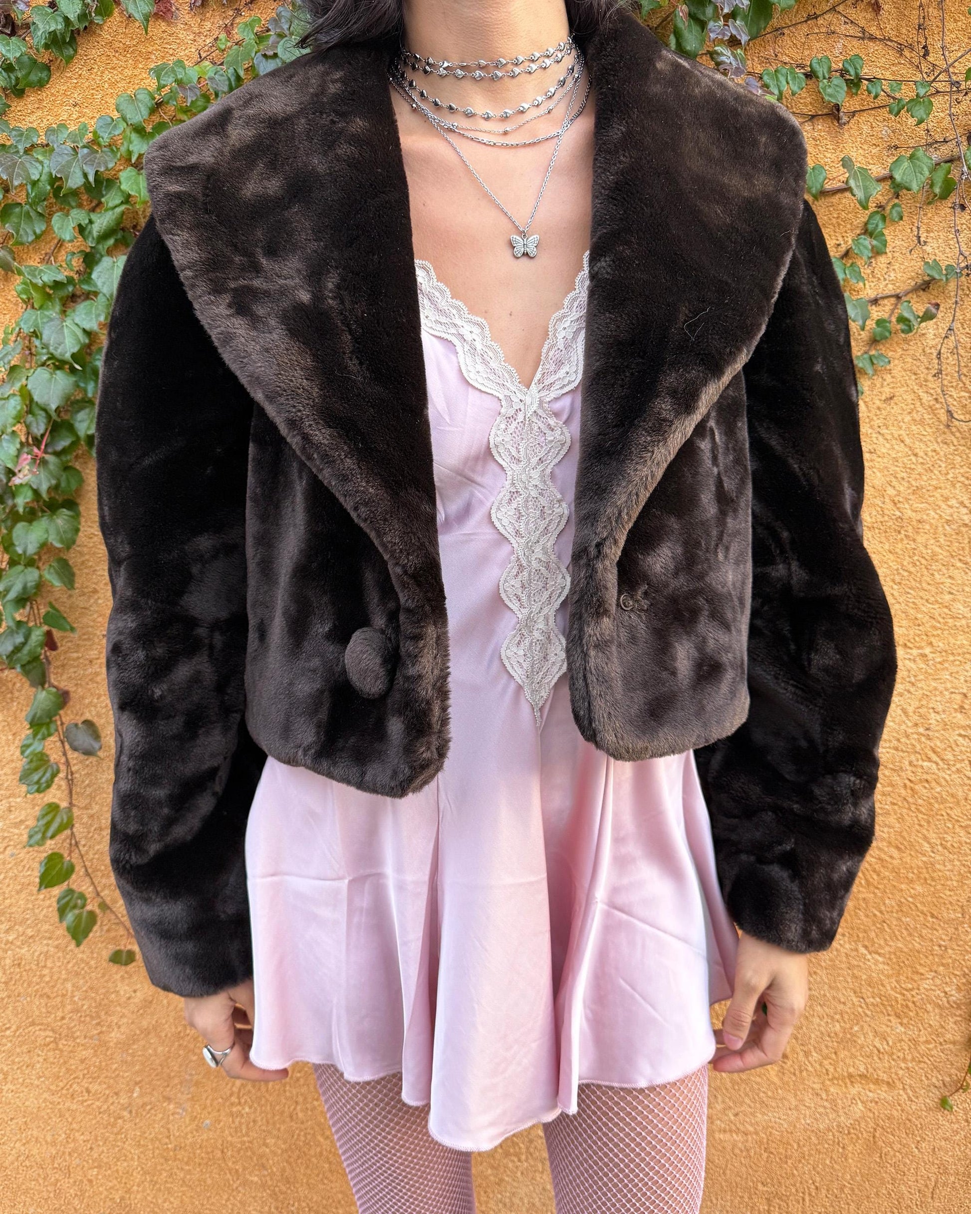 Vintage 90s dark brown faux fur cropped jacket featuring an exaggerated wide collar and a single hook-button closure. Soft, plush, and luxurious, it adds instant elegance to formal winter outfits and is perfect for gala events, prom nights, or refined evening layering. The cropped cut balances the dramatic collar, creating a chic silhouette that elevates dresses or slip styles with minimal effort. Made in Spain. Excellent vintage condition.