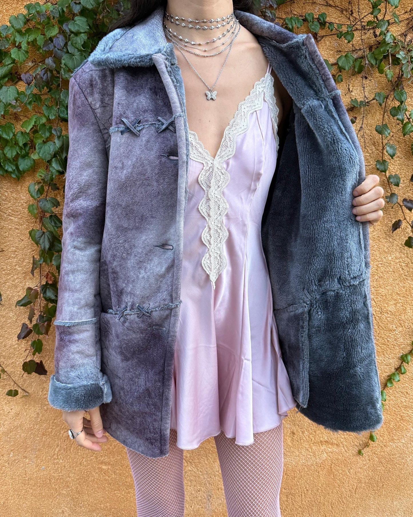 Vintage 2000s faux shearling coat in a rare purple-blue-gray tie-dye abstract finish. Features a soft faux fur collar and cuffs, button closure, side pockets, and decorative criss-cross stitch detailing for a dystopic, cyber-grunge aesthetic. The brushed faux-suede surface gives it a distressed Y2K look, while the straight silhouette makes it easy for winter layering and festival styling. A standout early-2000s piece for streetwear, weird-girl outfits, and bold cold-weather looks.