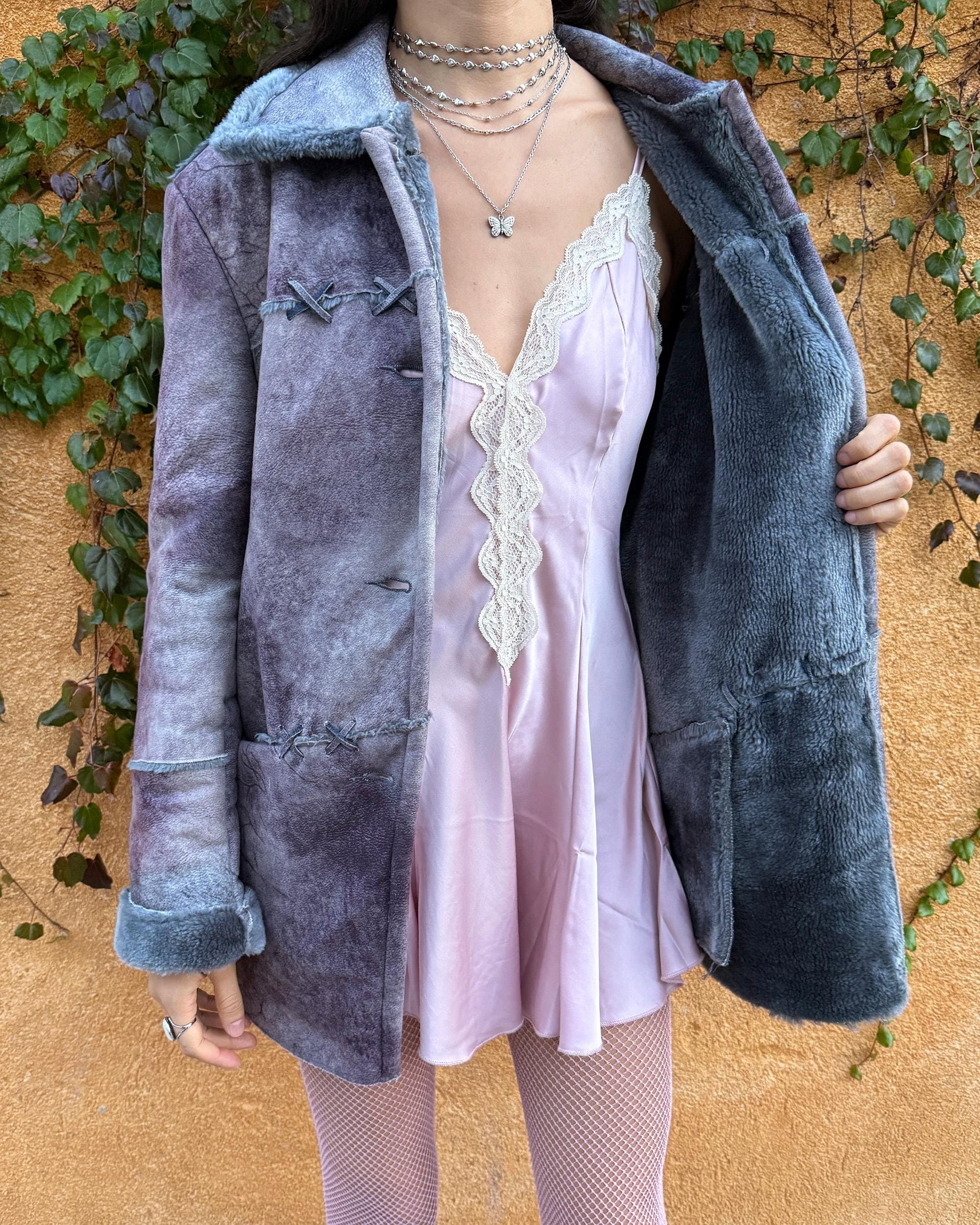 Vintage 2000s faux shearling coat in a rare purple-blue-gray tie-dye abstract finish. Features a soft faux fur collar and cuffs, button closure, side pockets, and decorative criss-cross stitch detailing for a dystopic, cyber-grunge aesthetic. The brushed faux-suede surface gives it a distressed Y2K look, while the straight silhouette makes it easy for winter layering and festival styling. A standout early-2000s piece for streetwear, weird-girl outfits, and bold cold-weather looks.