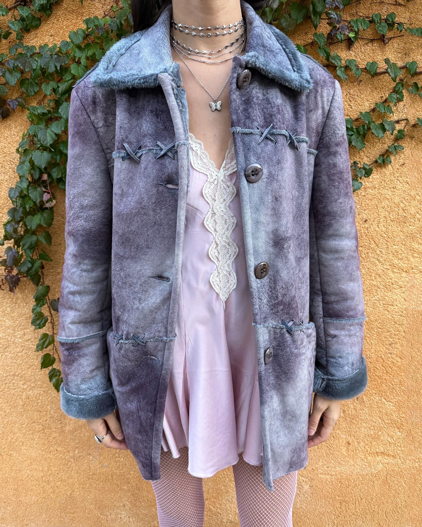 Vintage 2000s faux shearling coat in a rare purple-blue-gray tie-dye abstract finish. Features a soft faux fur collar and cuffs, button closure, side pockets, and decorative criss-cross stitch detailing for a dystopic, cyber-grunge aesthetic. The brushed faux-suede surface gives it a distressed Y2K look, while the straight silhouette makes it easy for winter layering and festival styling. A standout early-2000s piece for streetwear, weird-girl outfits, and bold cold-weather looks.