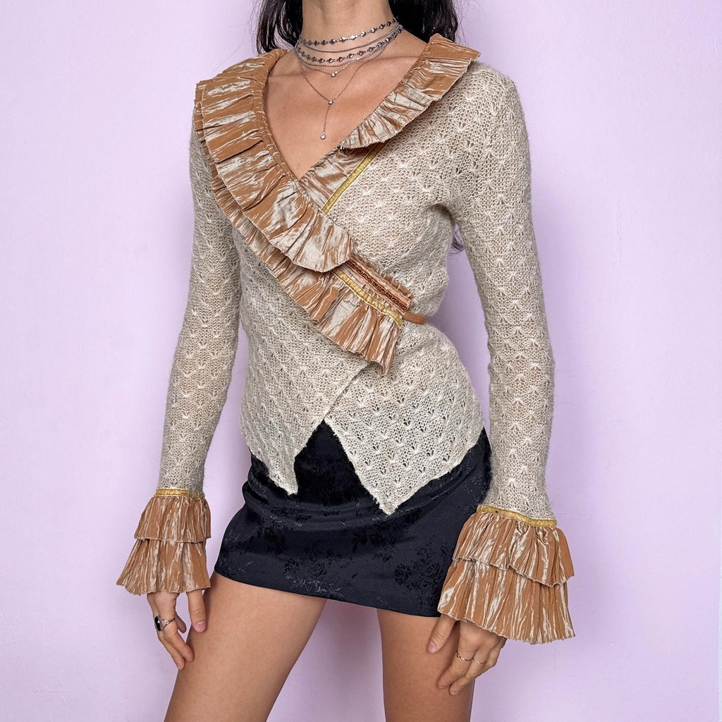 Vintage 2000s beige open-knit wrap cardigan with a dramatic ruffle neckline and tiered mustard-tone ruffle cuffs. Features an elegant tie-back closure, creating a fitted silhouette that highlights the waist. The extravagant design blends romantic, rococo-inspired detailing with a glamorous Y2K formal aesthetic, perfect for event nights, diva moments, or elevated evening styling. Made in France from an acrylic mohair polyester blend. Excellent vintage condition.