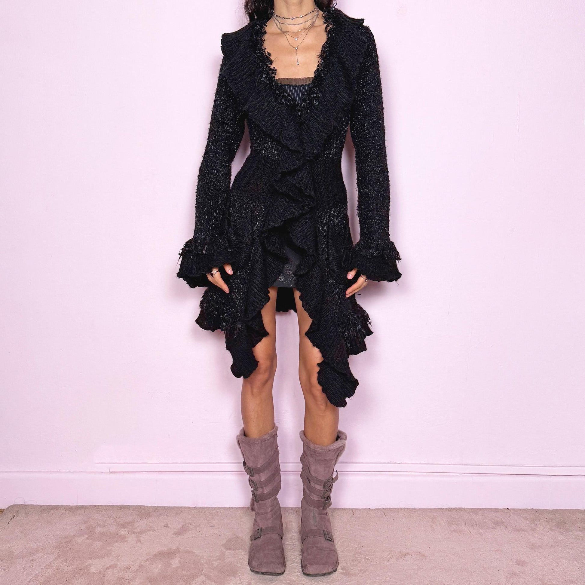 Witchy vintage 2000s black longline cardigan with dramatic ruffle neckline and dark romantic rococo style. Features bell sleeves with ruffle cuffs, two-button front closure, pockets, and asymmetric pointy hem. Whimsical fairycore silhouette, stretchy fabric for cozy winter layering. Made from polyester acrylic blend. Great vintage condition.