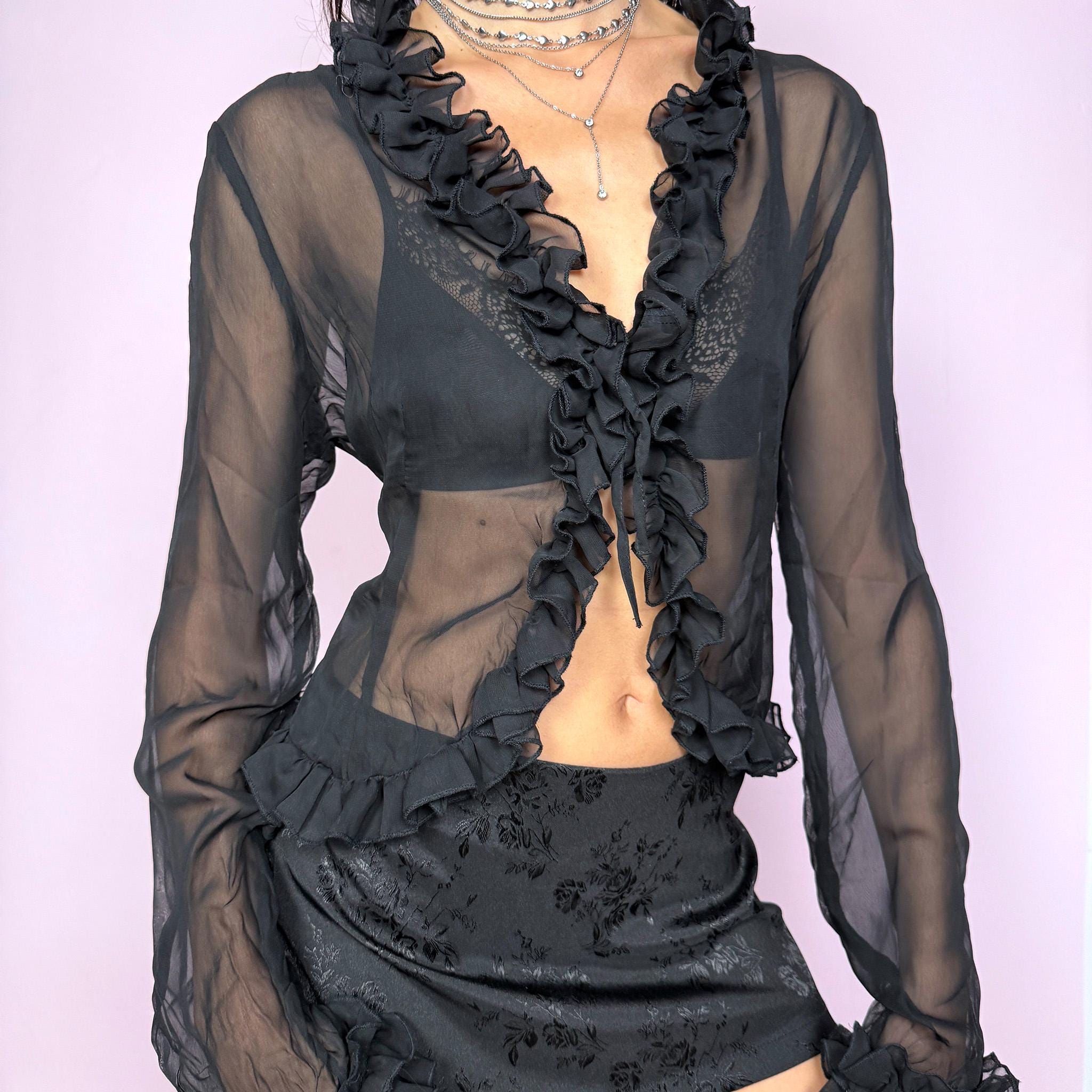 This vintage 2000s black semi-sheer top features long sleeves, a tie-front closure and a gathered ruffle neckline with matching ruffled cuffs. The lightweight fabric drapes softly with no stretch, creating an elegant dark romance look perfect for party nights, layering, or styling as a bolero-style blouse. A flattering statement piece that elevates evening outfits. Excellent vintage condition.