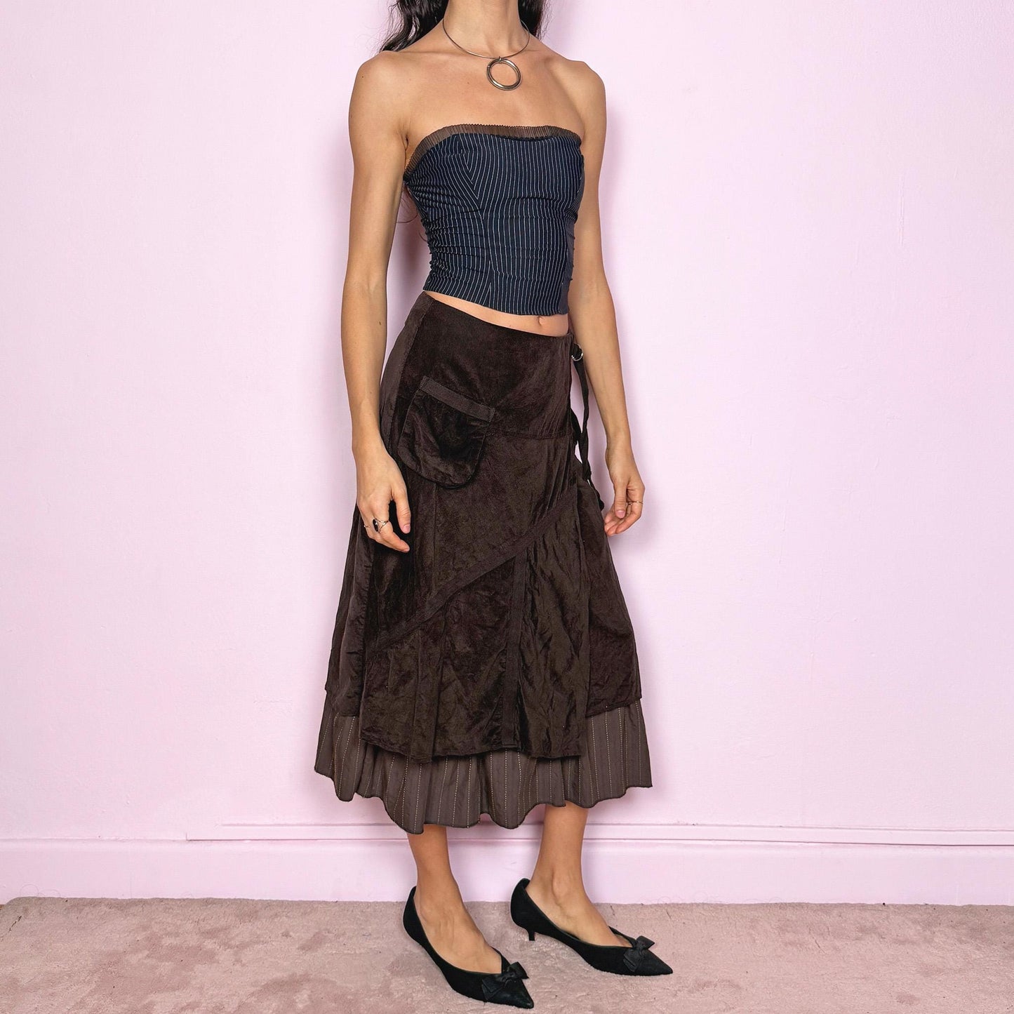 Vintage 2000s dark brown midi skirt with a layered wrap design and ruffled striped hem. Features decorative tie details, a back zipper closure, and a pocket for a deconstructed look. Ideal for earthy fairycore, bohemian, avant-garde, or cyber futuristic styling. Can be worn mid to low rise for size XXS–XS or high waisted for size S. Made from corduroy cotton and polyester. Great vintage condition.