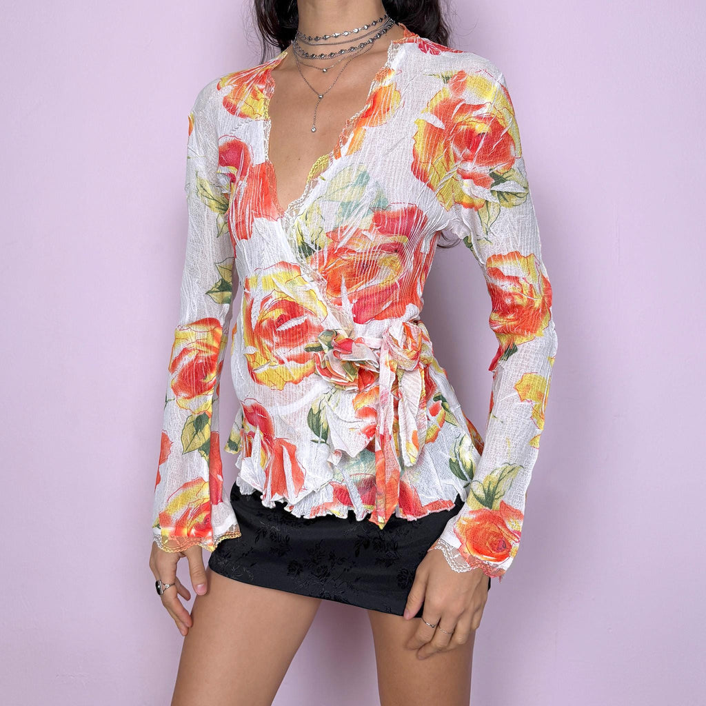 Dreamy vintage 2000s white wrap tie blouse with orange, red, and yellow rose floral print. Features lace trim, bell sleeves, crinkle pleated fabric, and rosette appliqué detail. Stunning deep V-neck top perfect for spring summer parties, formal or outdoor events. Made from stretchy polyester by a French brand. Excellent vintage condition.