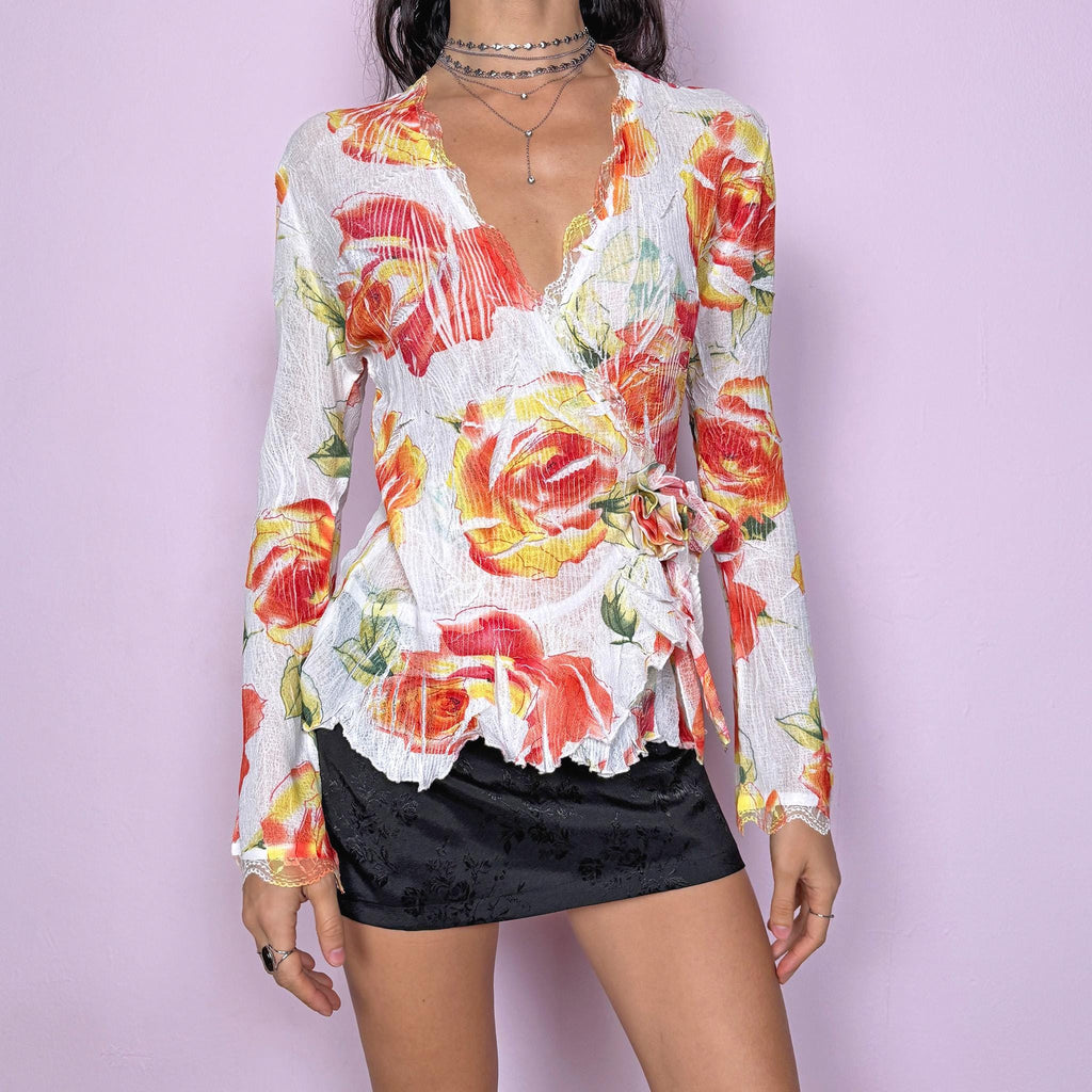 Dreamy vintage 2000s white wrap tie blouse with orange, red, and yellow rose floral print. Features lace trim, bell sleeves, crinkle pleated fabric, and rosette appliqué detail. Stunning deep V-neck top perfect for spring summer parties, formal or outdoor events. Made from stretchy polyester by a French brand. Excellent vintage condition.