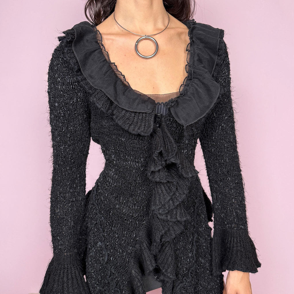 Witchy vintage 2000s black knit cardigan with a dramatic ruffle neckline and dark romantic rococo style. Features bell sleeves, toggle front closure, and an asymmetric pointy hem. Whimsical fairycore silhouette with stretchy fabric for cozy, extravagant winter layering. Made from a 50% polyamide, 30% wool, and 20% cotton blend. Great vintage condition.