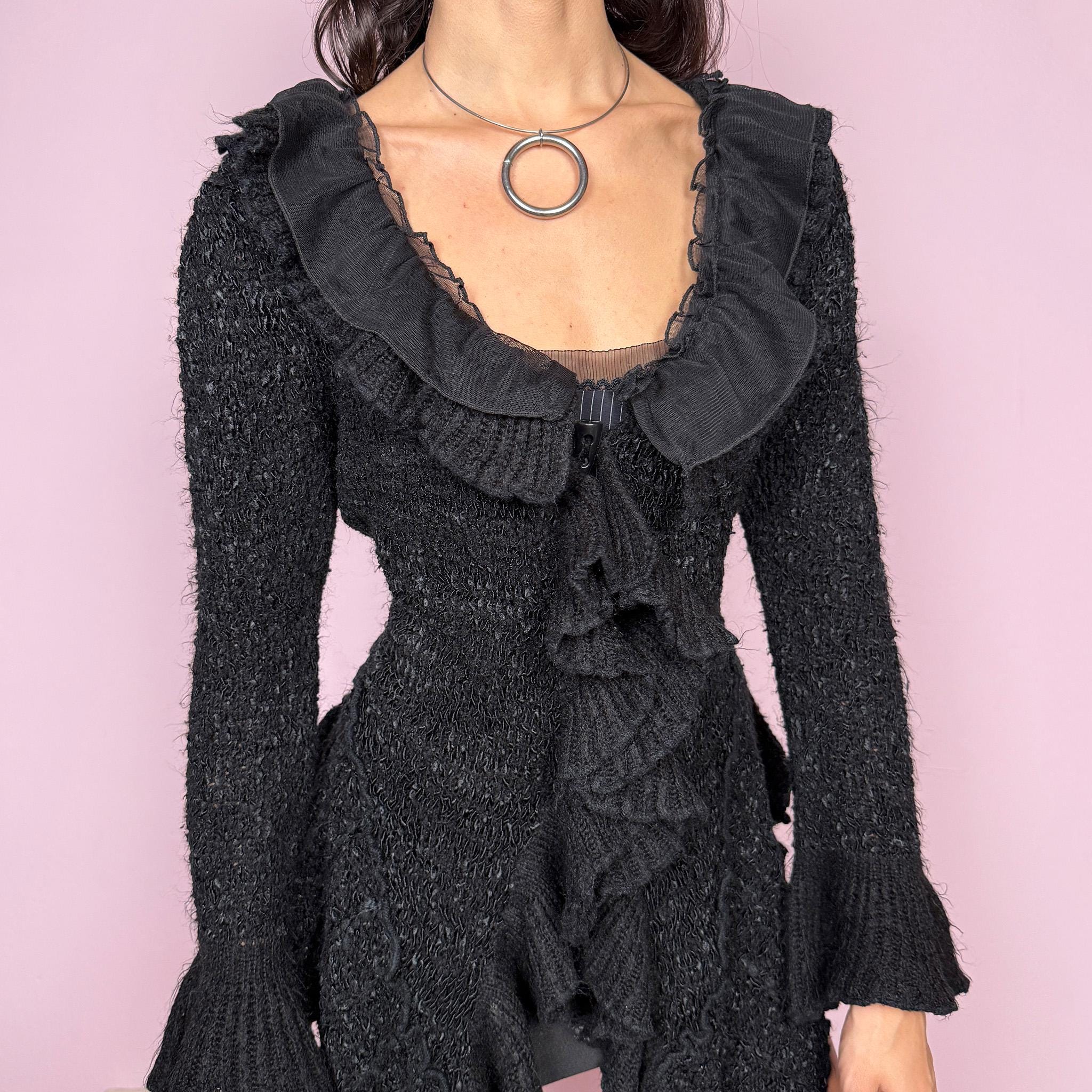 Witchy vintage 2000s black knit cardigan with a dramatic ruffle neckline and dark romantic rococo style. Features bell sleeves, toggle front closure, and an asymmetric pointy hem. Whimsical fairycore silhouette with stretchy fabric for cozy, extravagant winter layering. Made from a 50% polyamide, 30% wool, and 20% cotton blend. Great vintage condition.