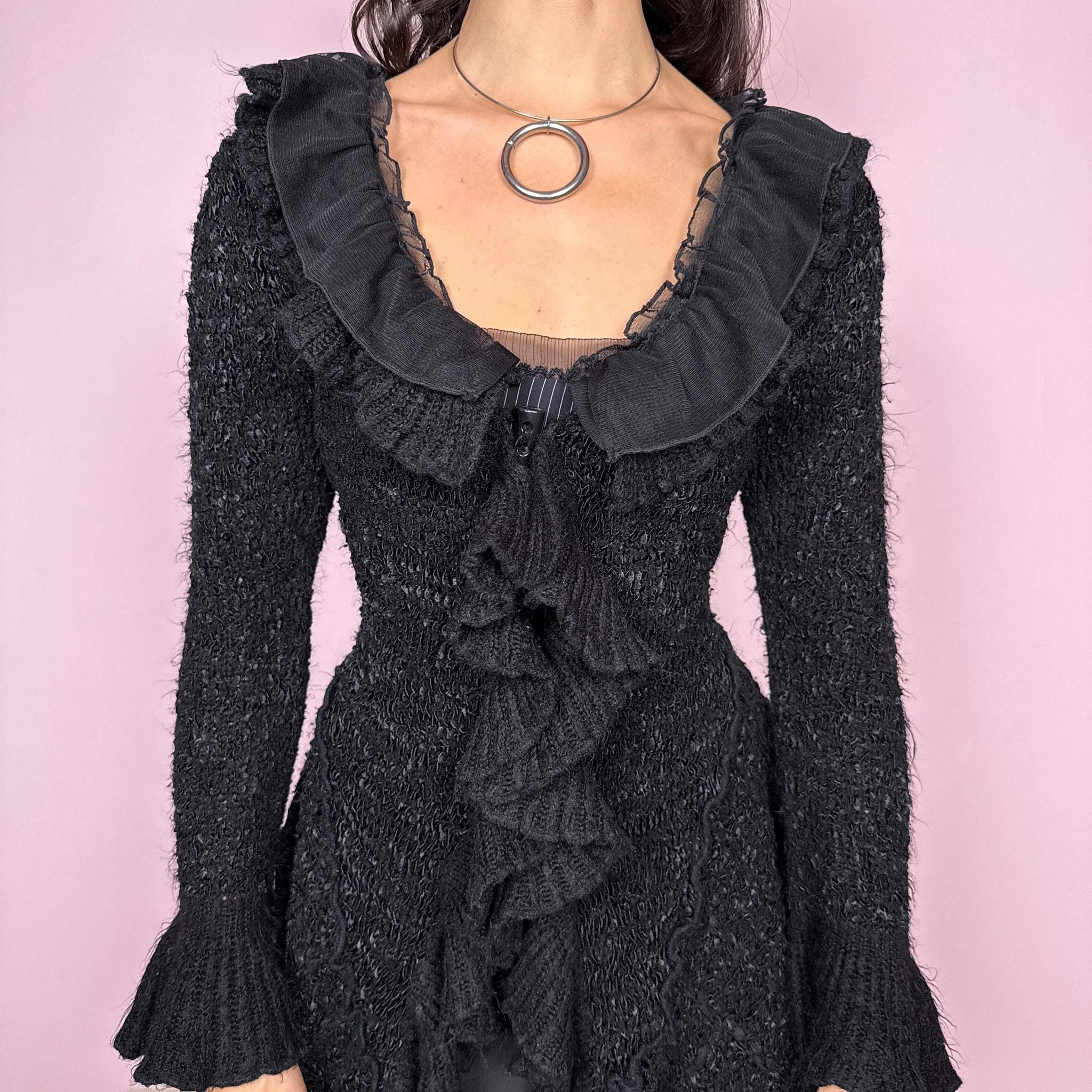 Witchy vintage 2000s black knit cardigan with a dramatic ruffle neckline and dark romantic rococo style. Features bell sleeves, toggle front closure, and an asymmetric pointy hem. Whimsical fairycore silhouette with stretchy fabric for cozy, extravagant winter layering. Made from a 50% polyamide, 30% wool, and 20% cotton blend. Great vintage condition.