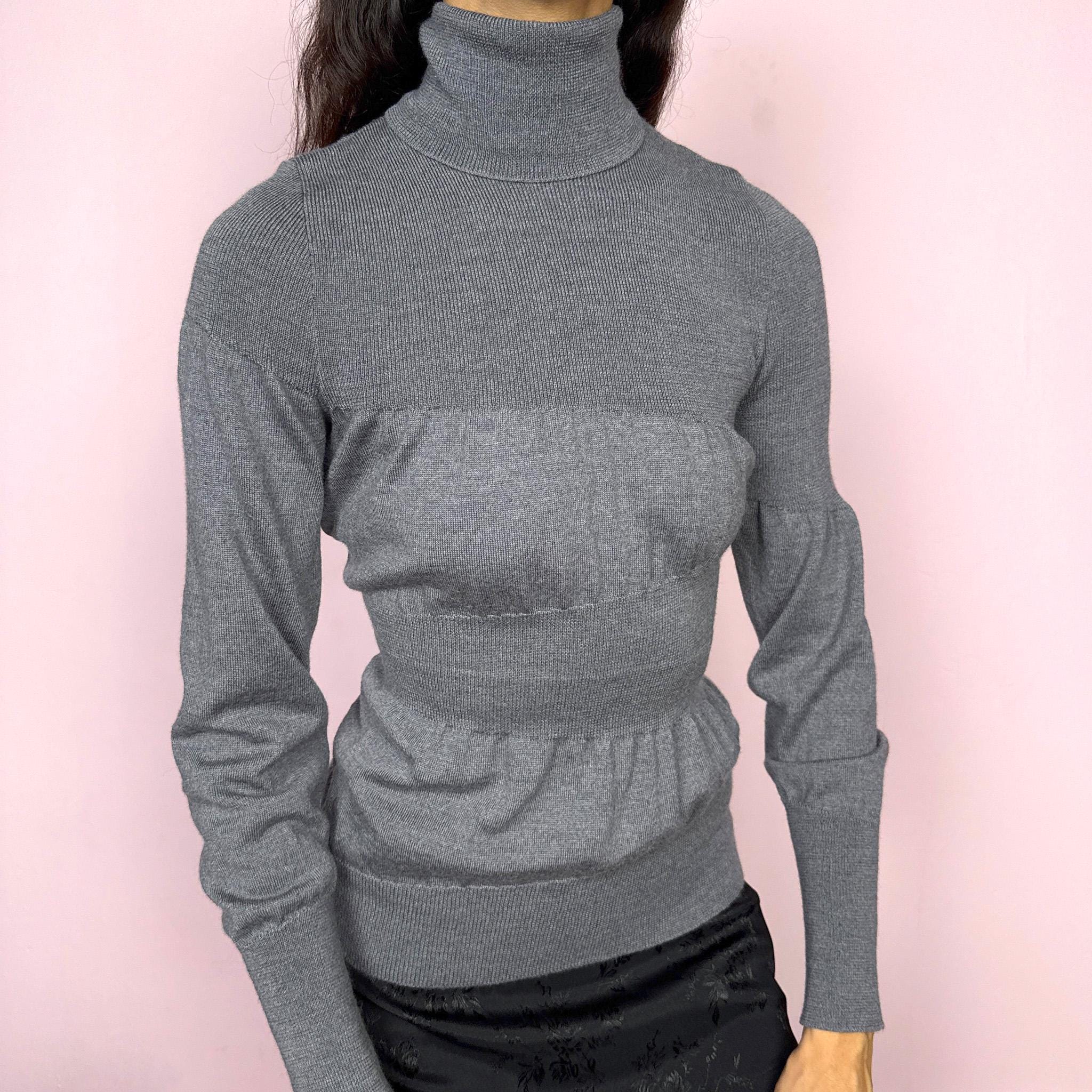Avant garde vintage 2000s Italian designer gray turtleneck sweater by Moschino Cheap and Chic, crafted from 100% virgin wool and made in Italy. Sculptural knit design with ballooned panels contrasted by fitted sections, creating subtle volume and structure. Clean design typical of Moschino’s early-2000s tailoring, where quality materials and sharp construction took priority over graphics. Perfect for minimal 90s, office siren, or elevated everyday styling. Excellent vintage condition.