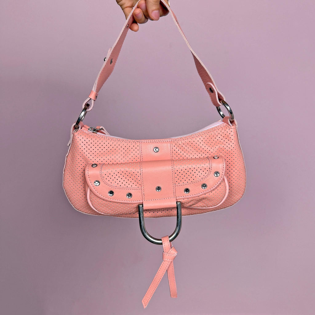 Vintage 2000s pink leather shoulder bag crafted in soft perforated leather with silver tone hardware and a structured baguette silhouette. Features a statement ring detail, front pocket accents with rhinestones, and a zip closure. A feminine yet edgy Y2K party statement piece. Made in Italy. Great vintage condition.